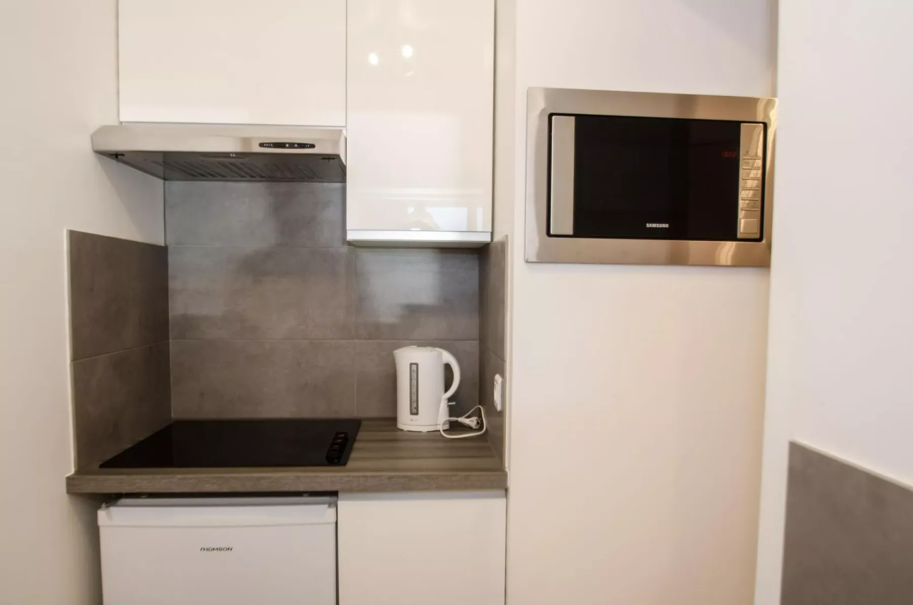 A compact kitchen area with a cooktop, kettle, and built-in microwave.