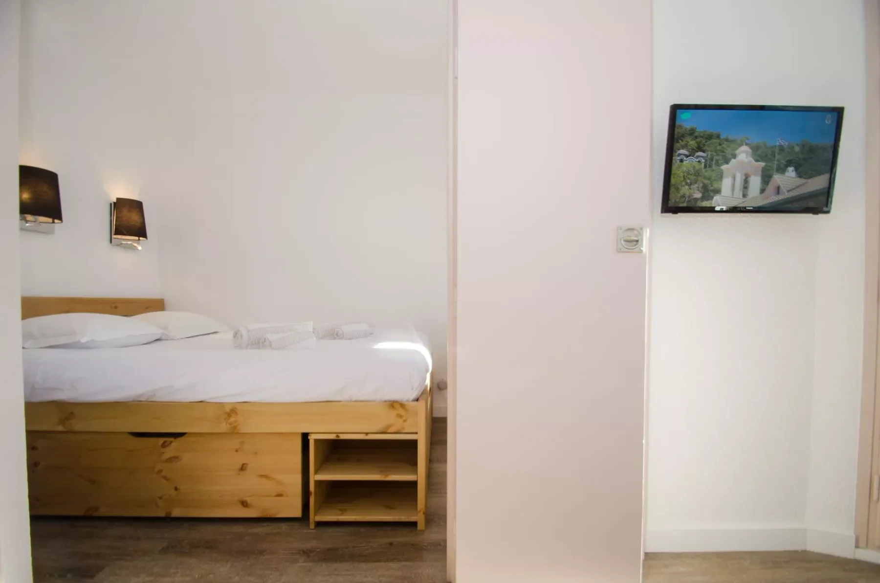 A bedroom with a wooden bed and a wall-mounted television.