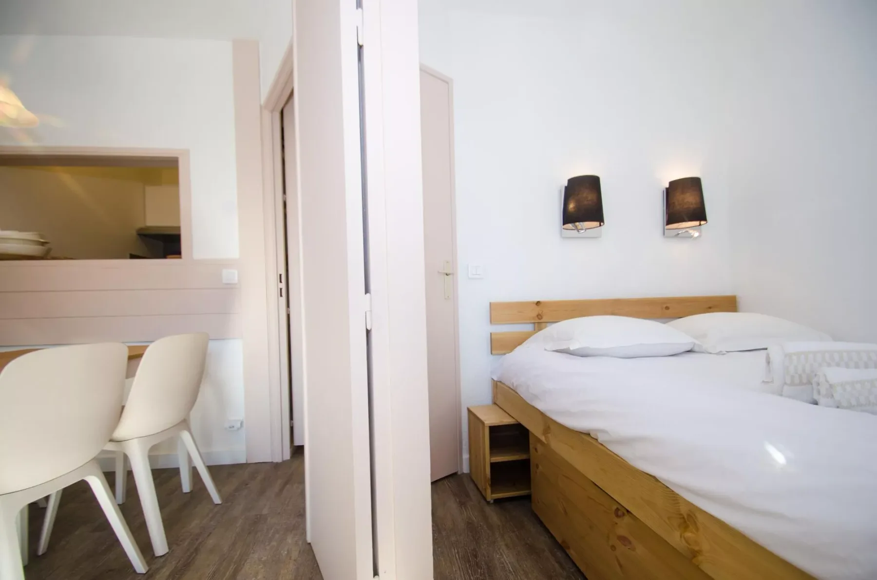 A bedroom with a wooden bed, white bedding, and two wall lights.