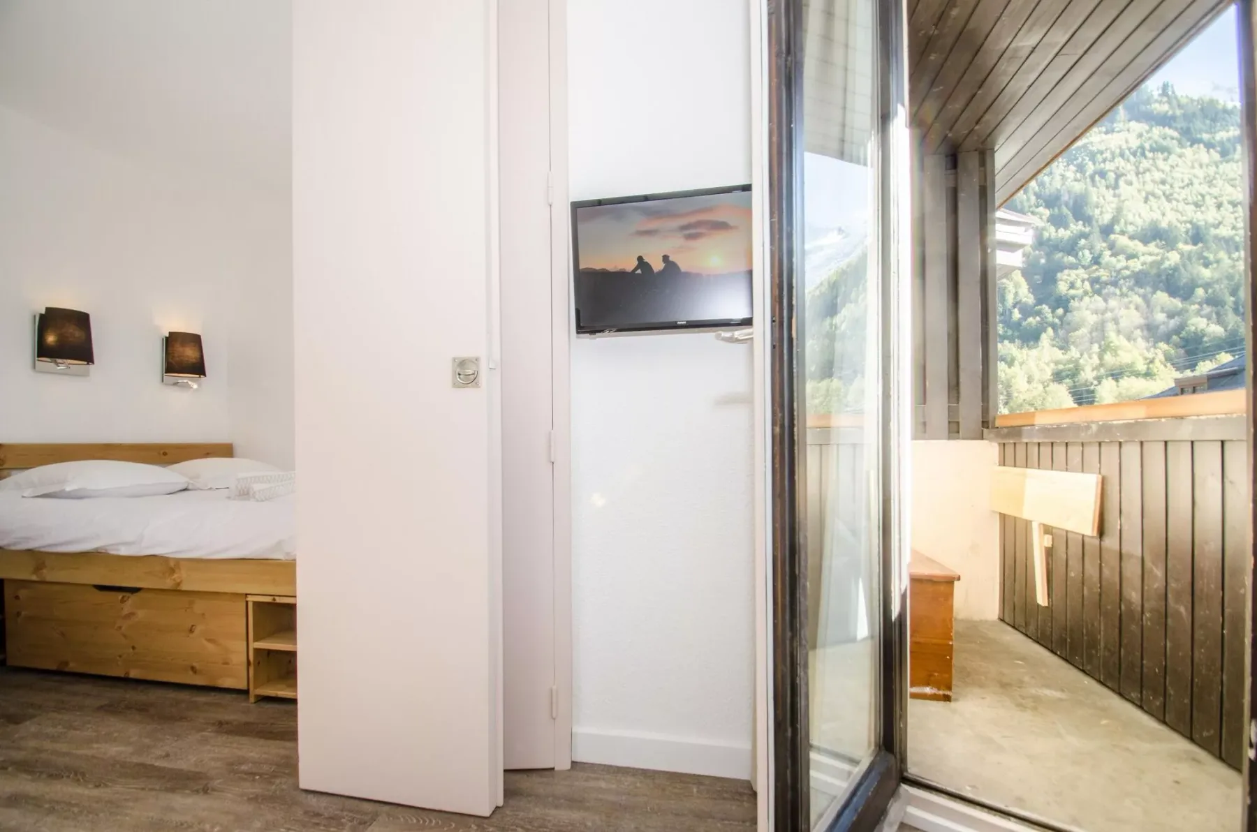 A bedroom opens onto a balcony with a view of a wooded hillside.