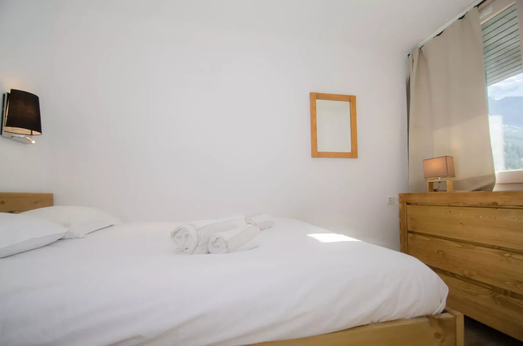 A bedroom with a neatly made bed and a wooden dresser beside the window.