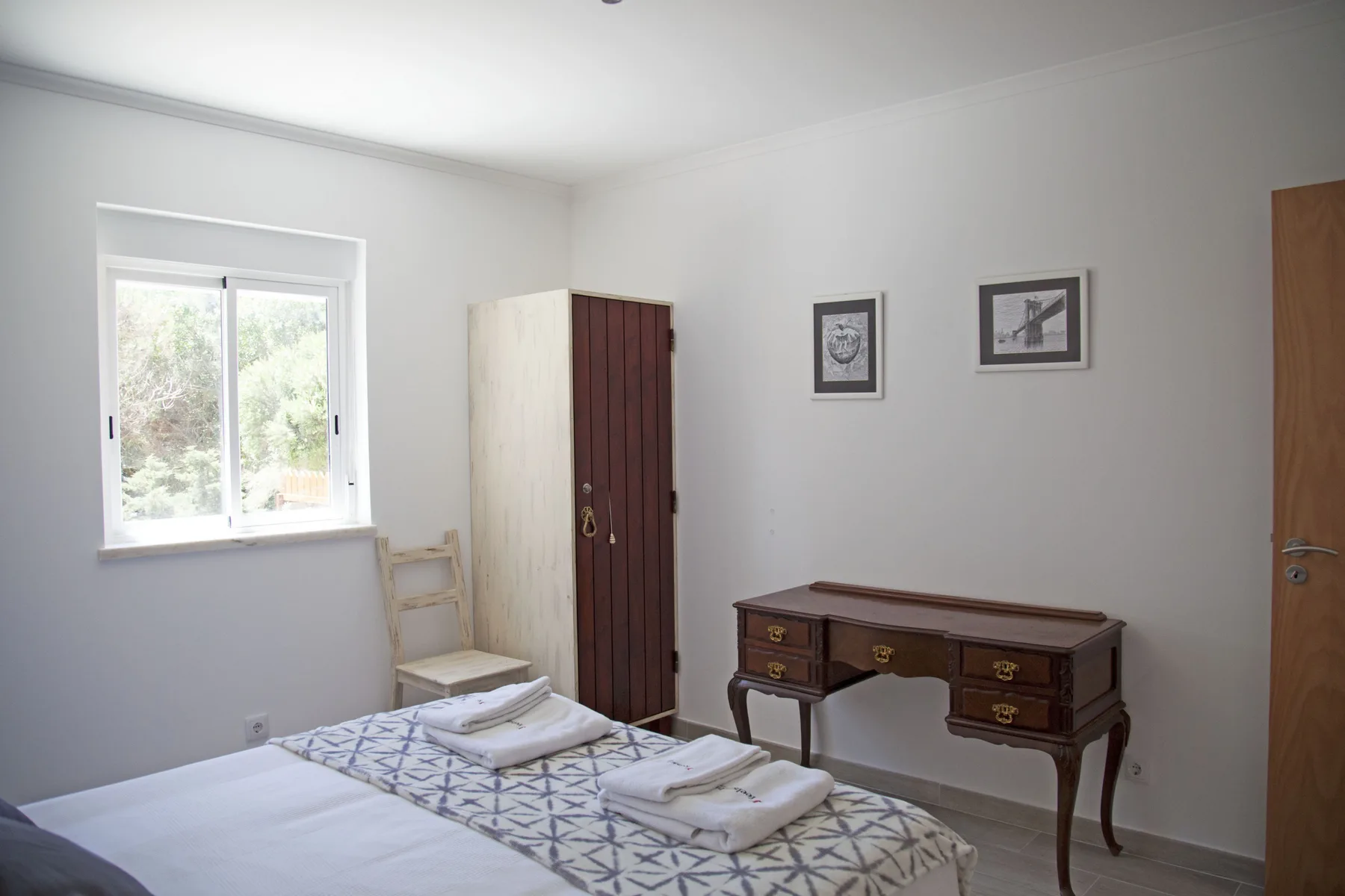 A bedroom with a bed, a writing desk, and a window overlooking greenery.
