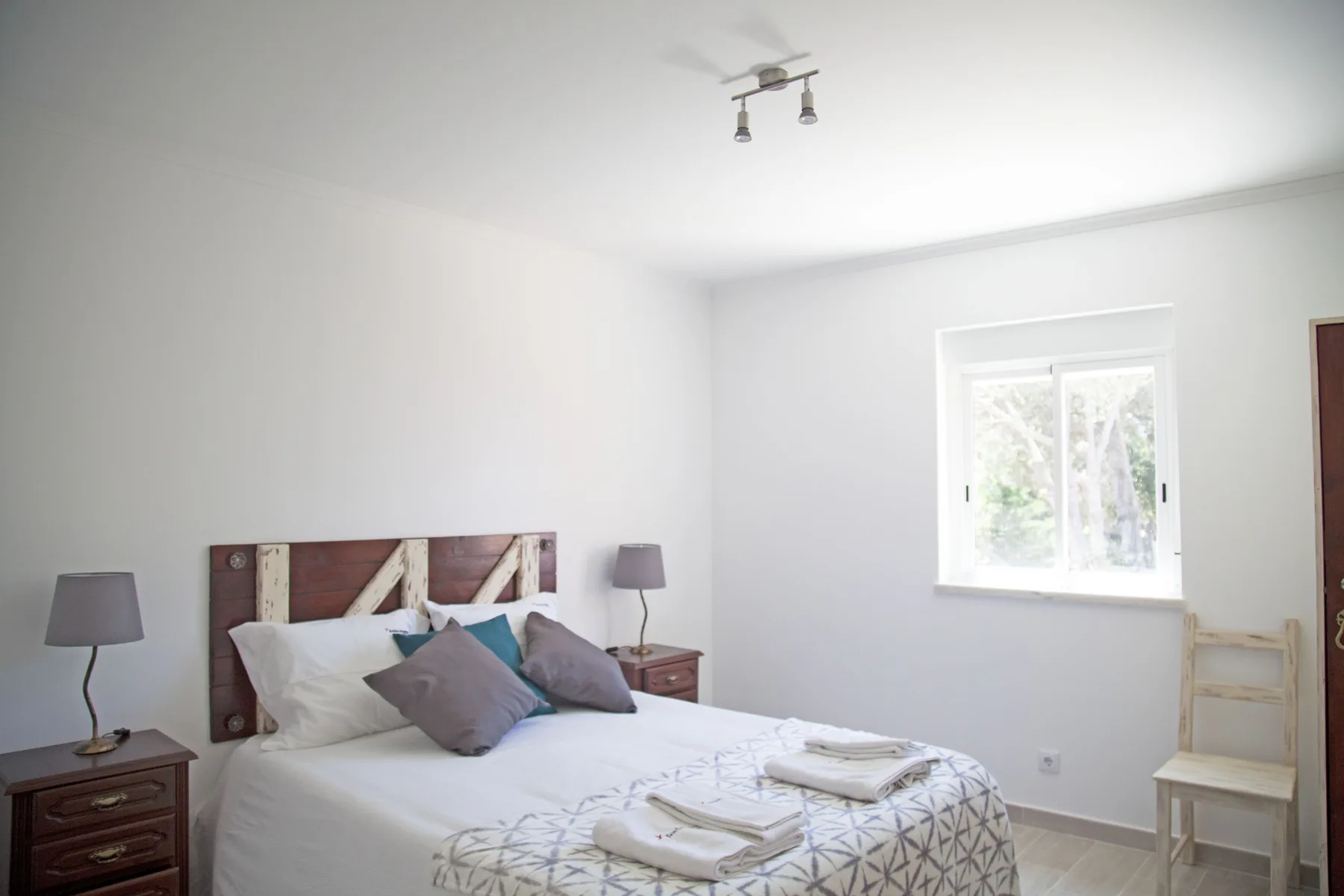 A bright bedroom with a bed, bedside tables, and a window.