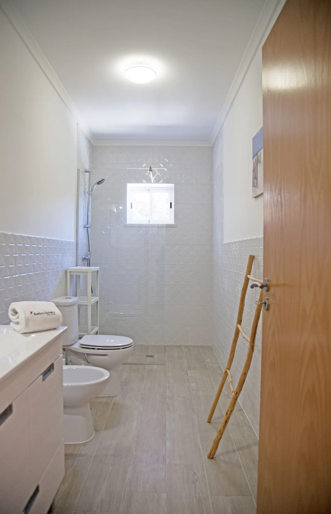 A bright bathroom with a shower, toilet, and small window.