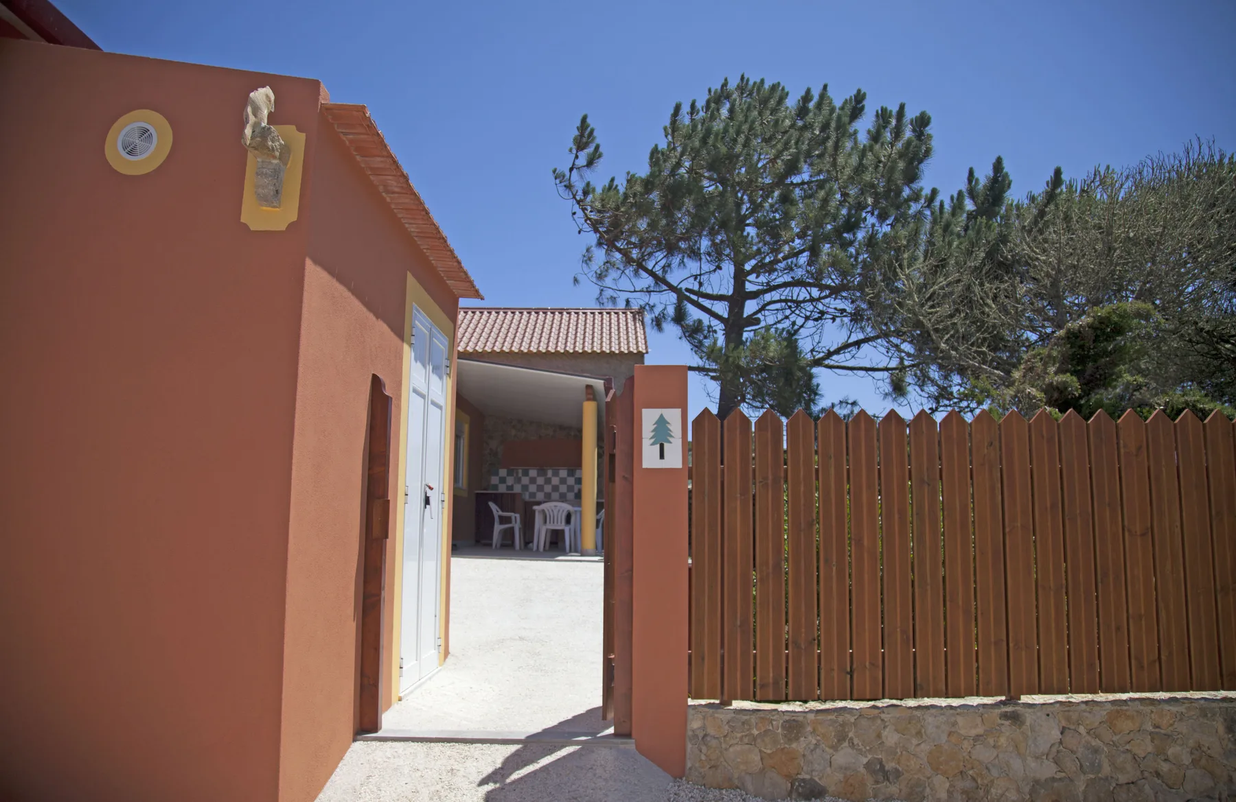 An exterior entrance opens onto a courtyard beside a wooden fence and trees.