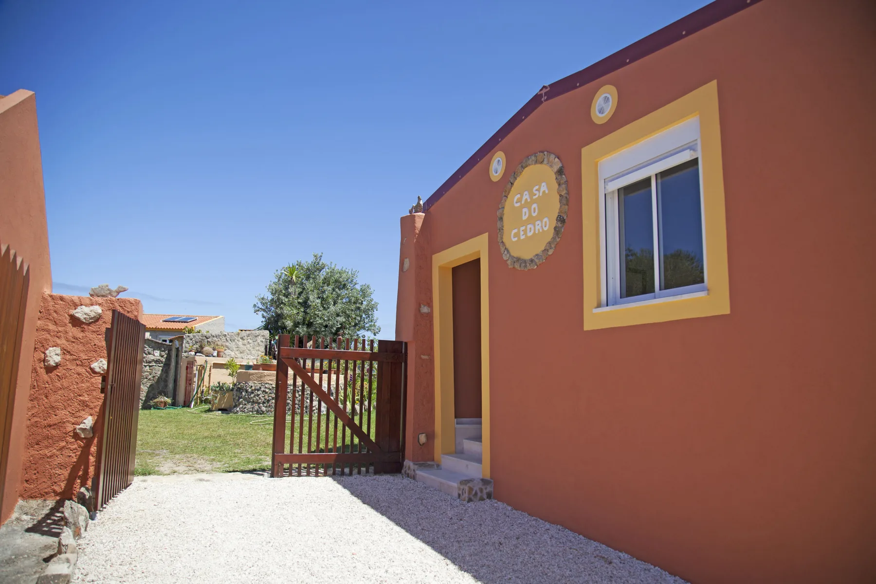 A gated house entrance opens onto a gravel path beside a small garden.