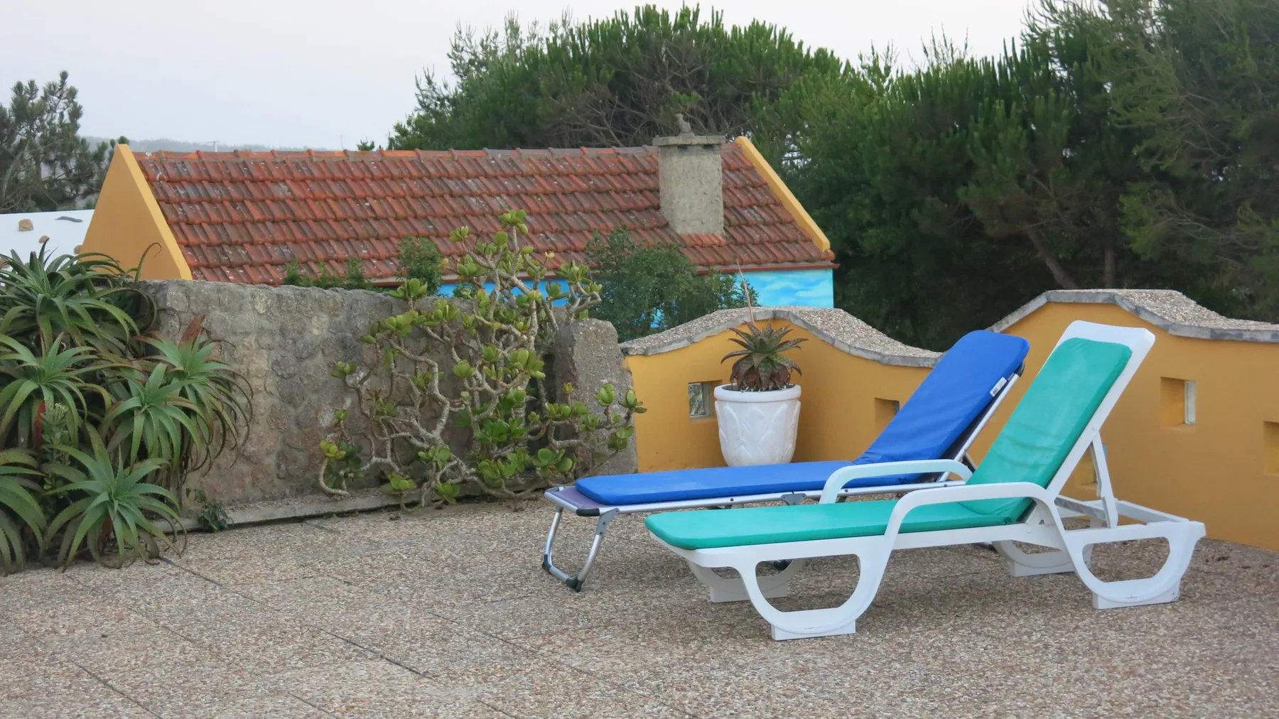 A sun terrace with two reclining loungers beside a low garden wall.