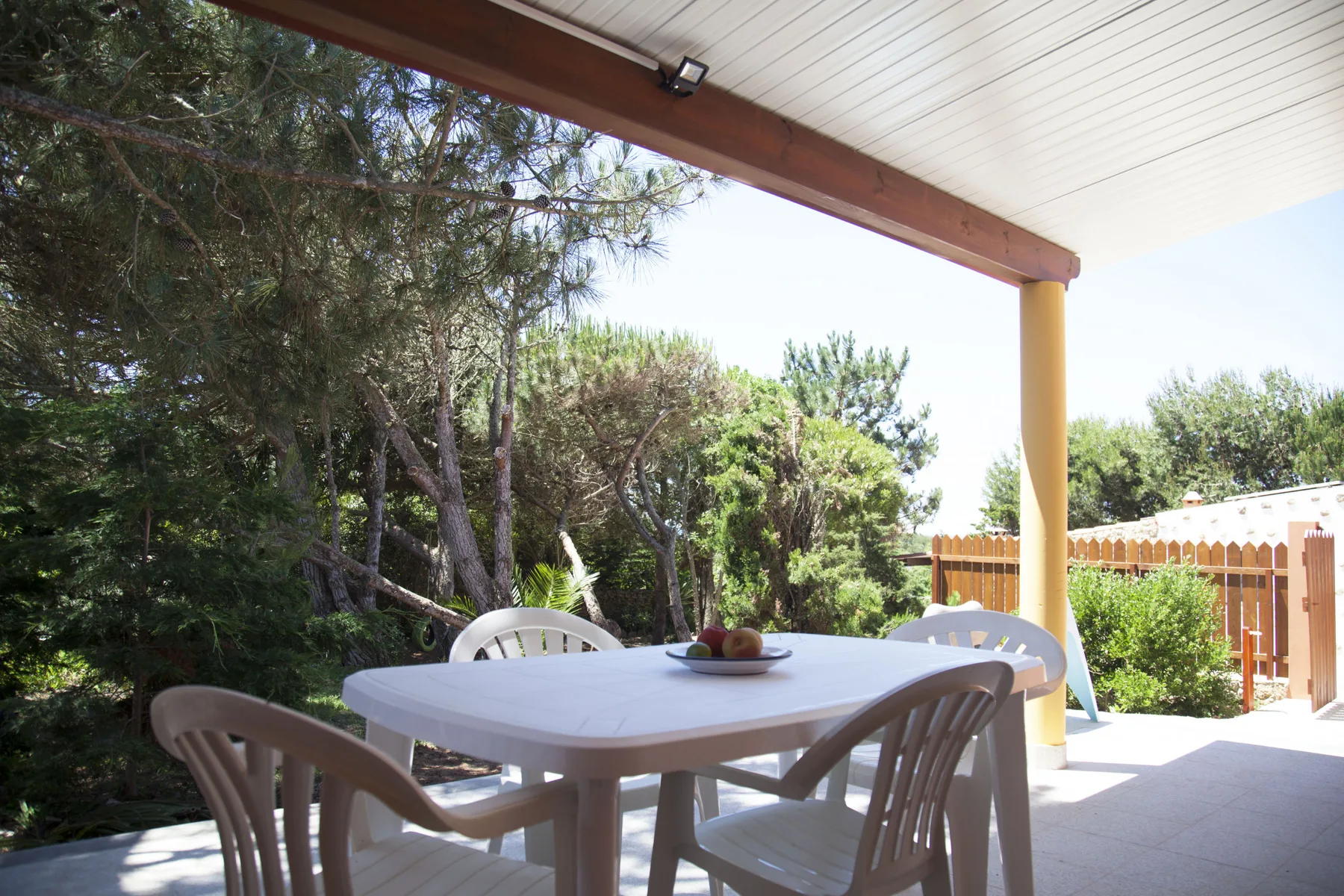 A covered outdoor dining area with a table and chairs overlooking leafy trees.
