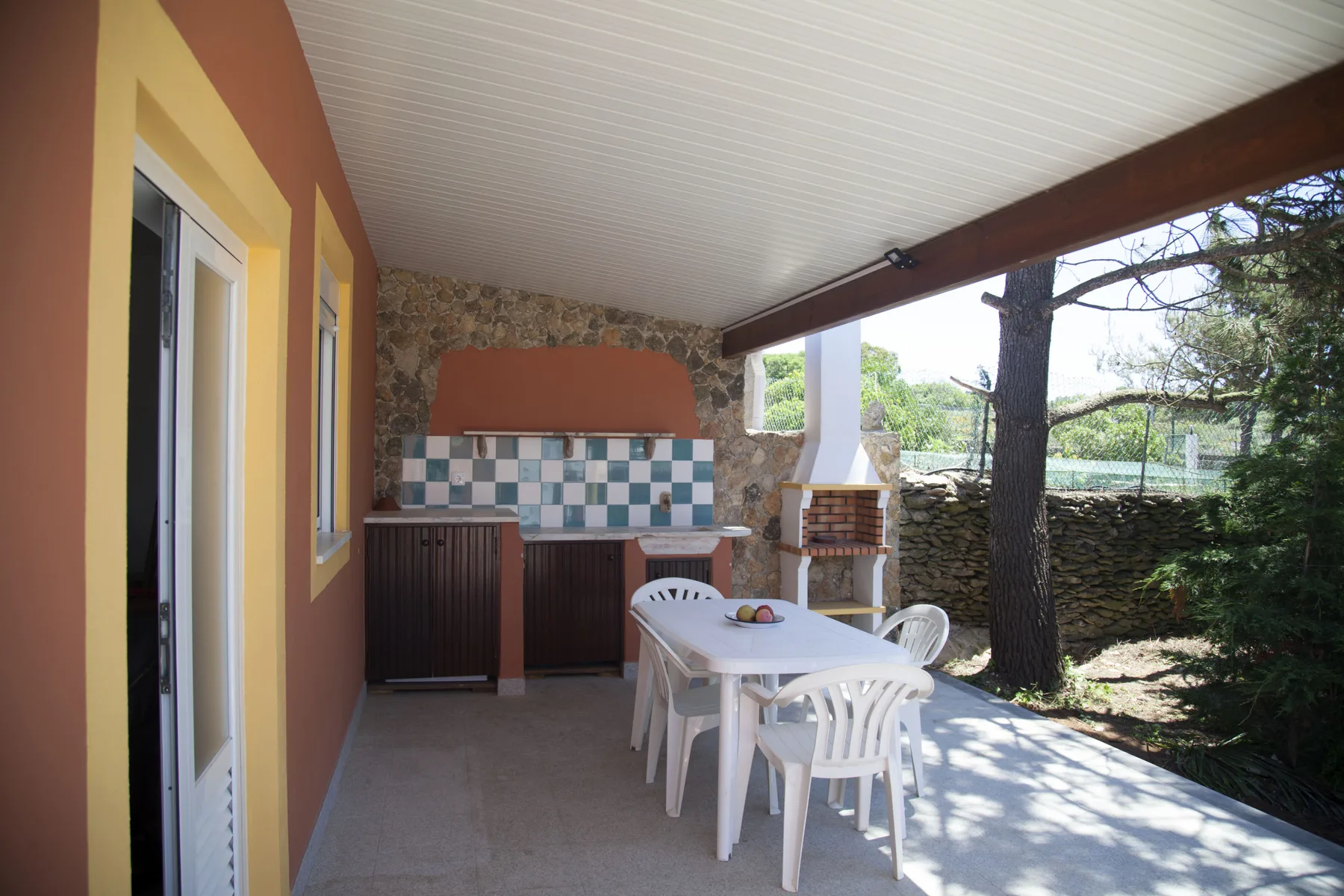 A covered outdoor dining area with a table, seating, and a built-in grill.