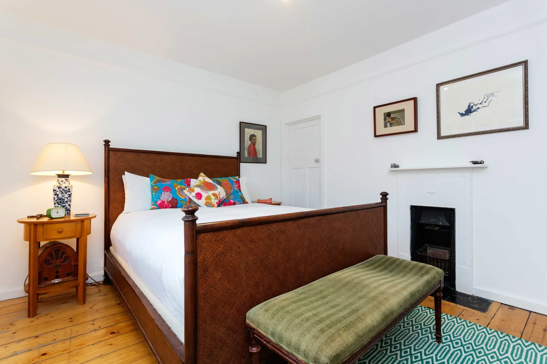 A bedroom with a wooden bed, colorful pillows, and a bench at the foot.