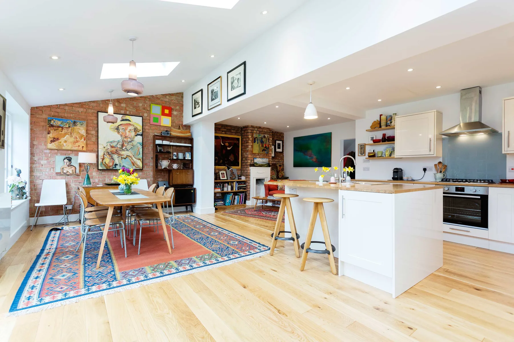 An open-plan dining and kitchen area with a wooden table and colorful rugs.