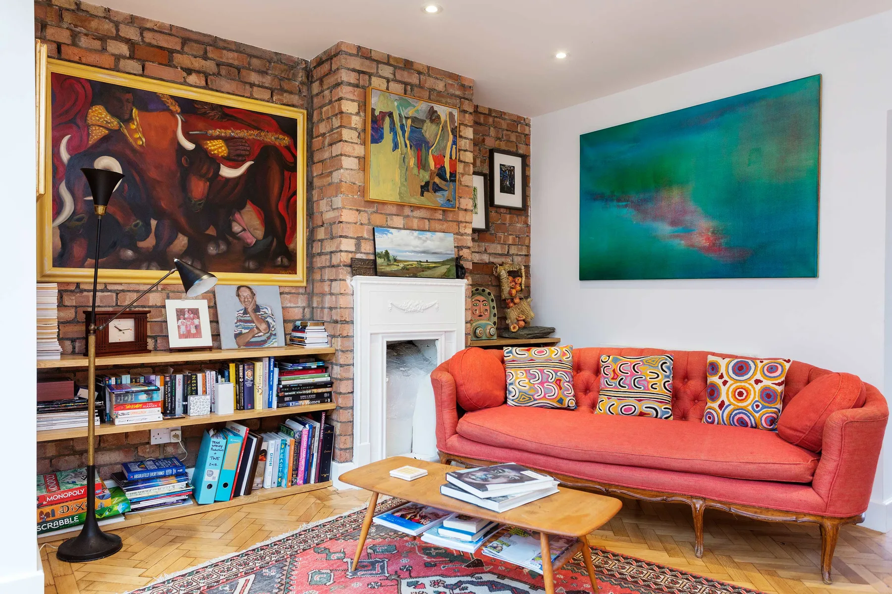 A colorful living room with a red sofa, bookshelves, and paintings.