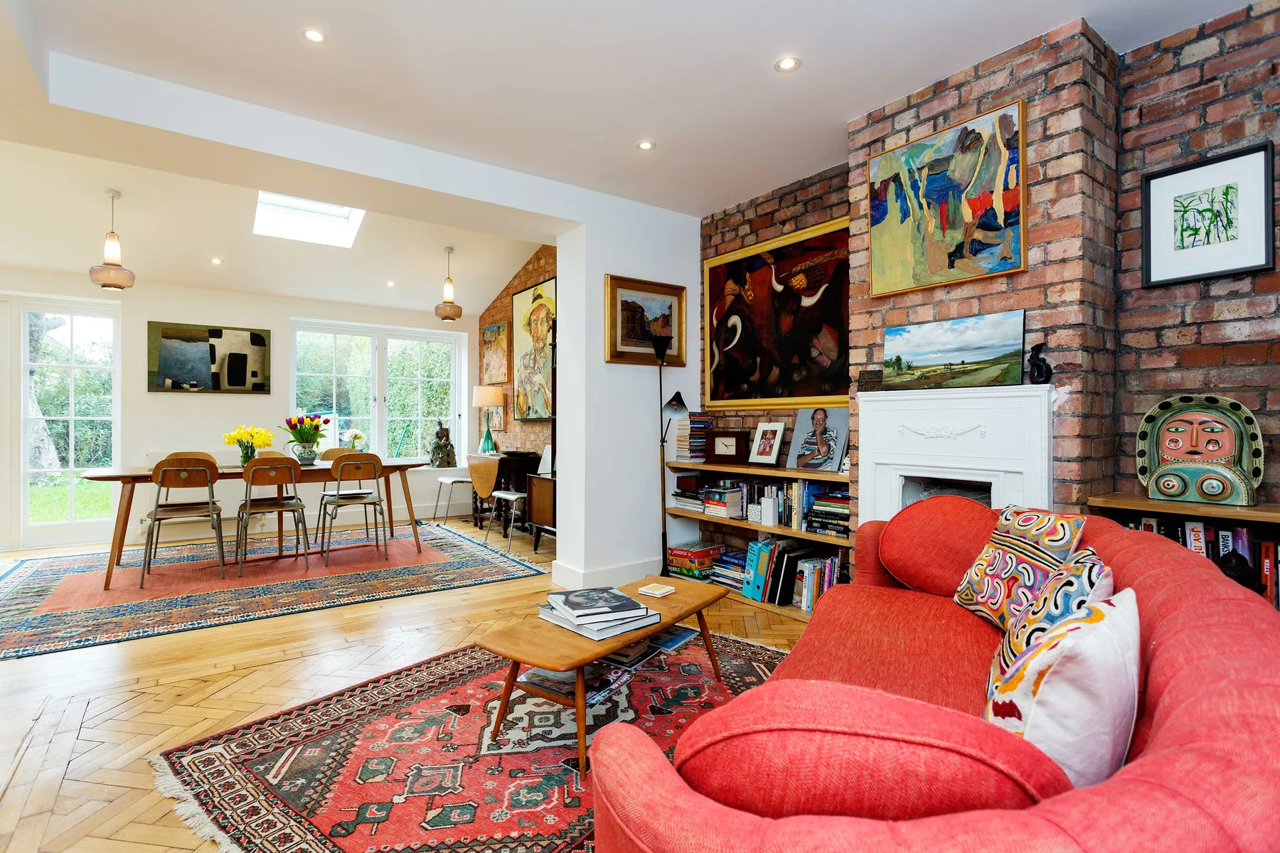 A living room with red seating, patterned rugs, and colorful artwork on brick walls.
