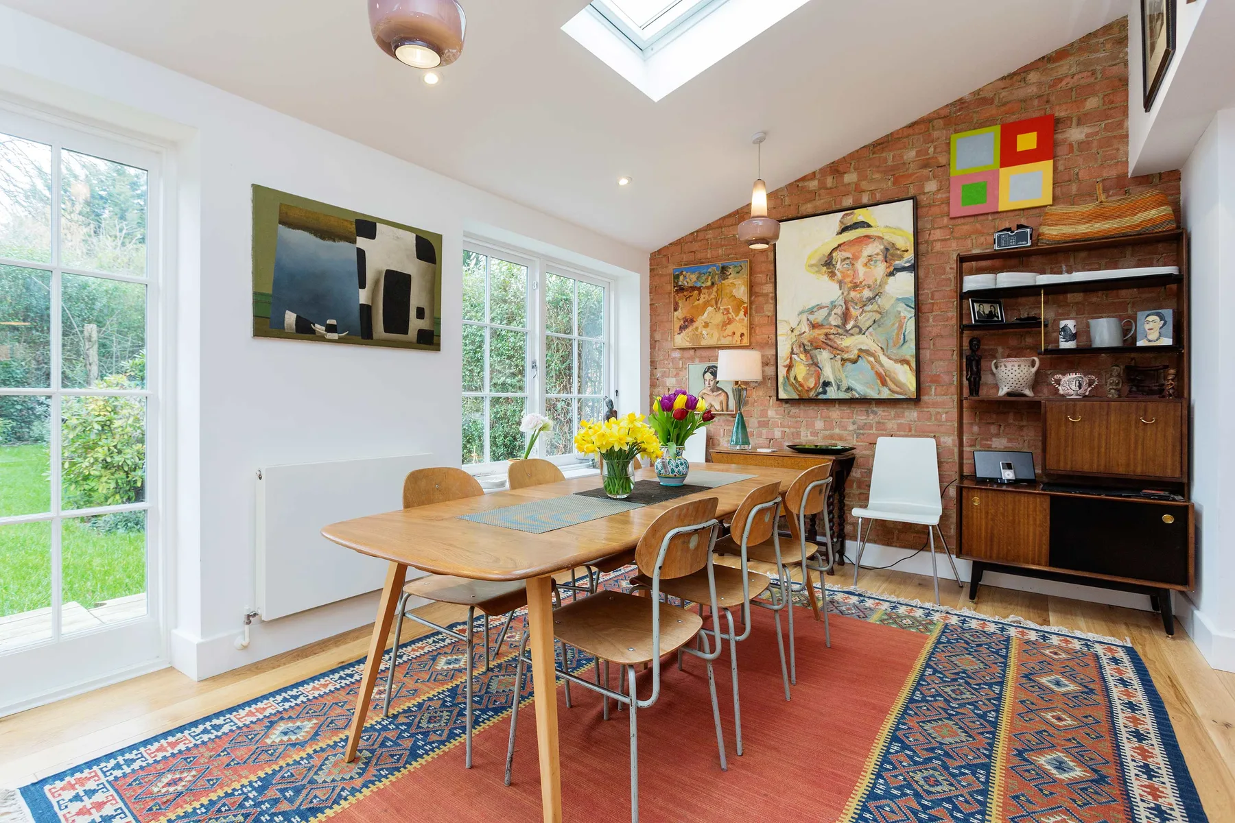 A bright dining area features a wooden table, chairs, and colorful artwork.