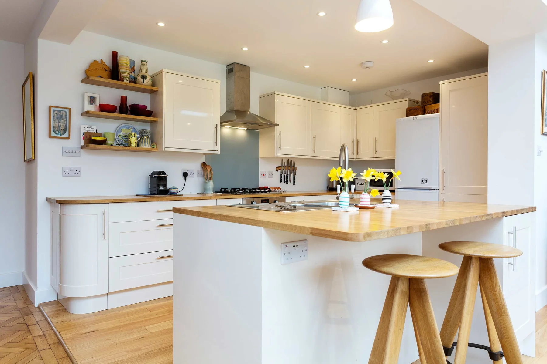 A bright kitchen with white cabinets, a central island, and wooden stools.