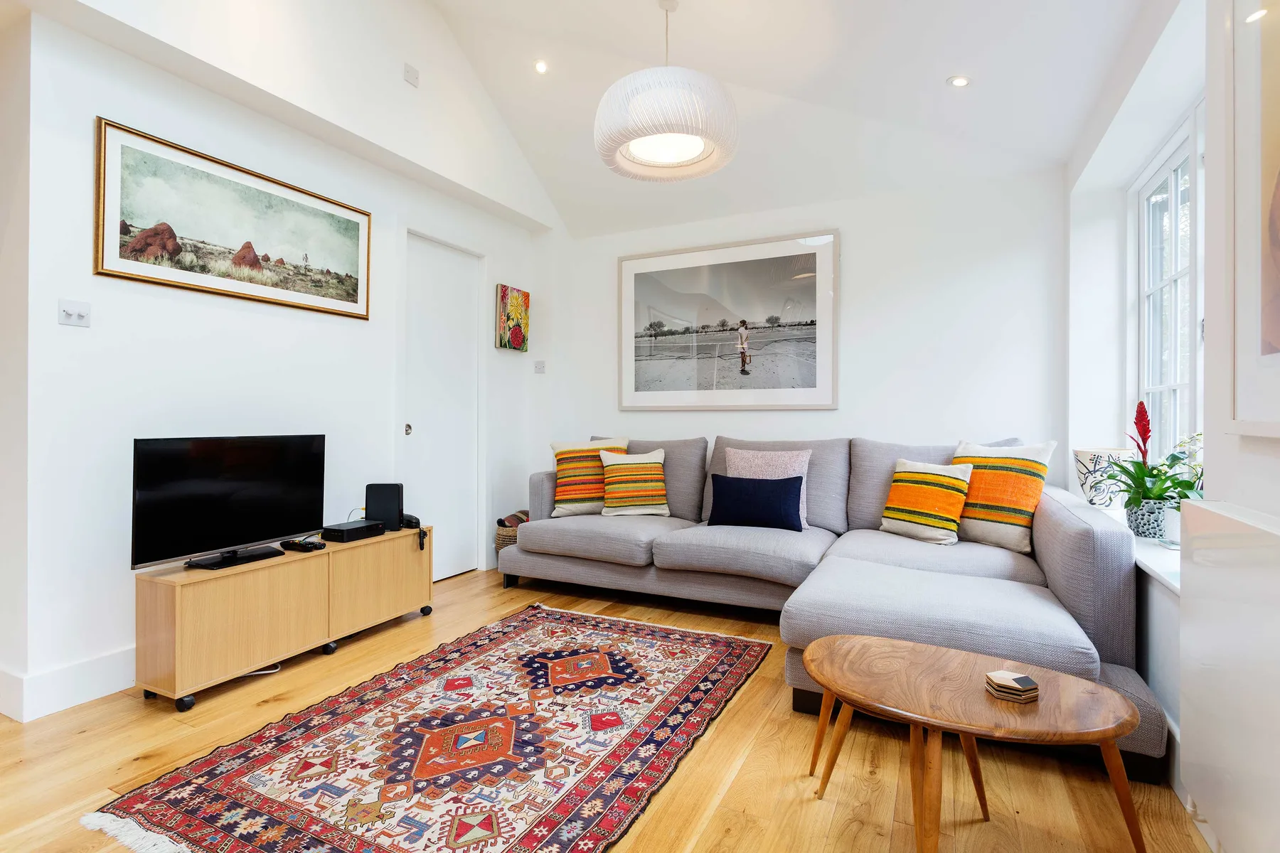 A bright living room with a gray sectional, colorful rug, and large windows.