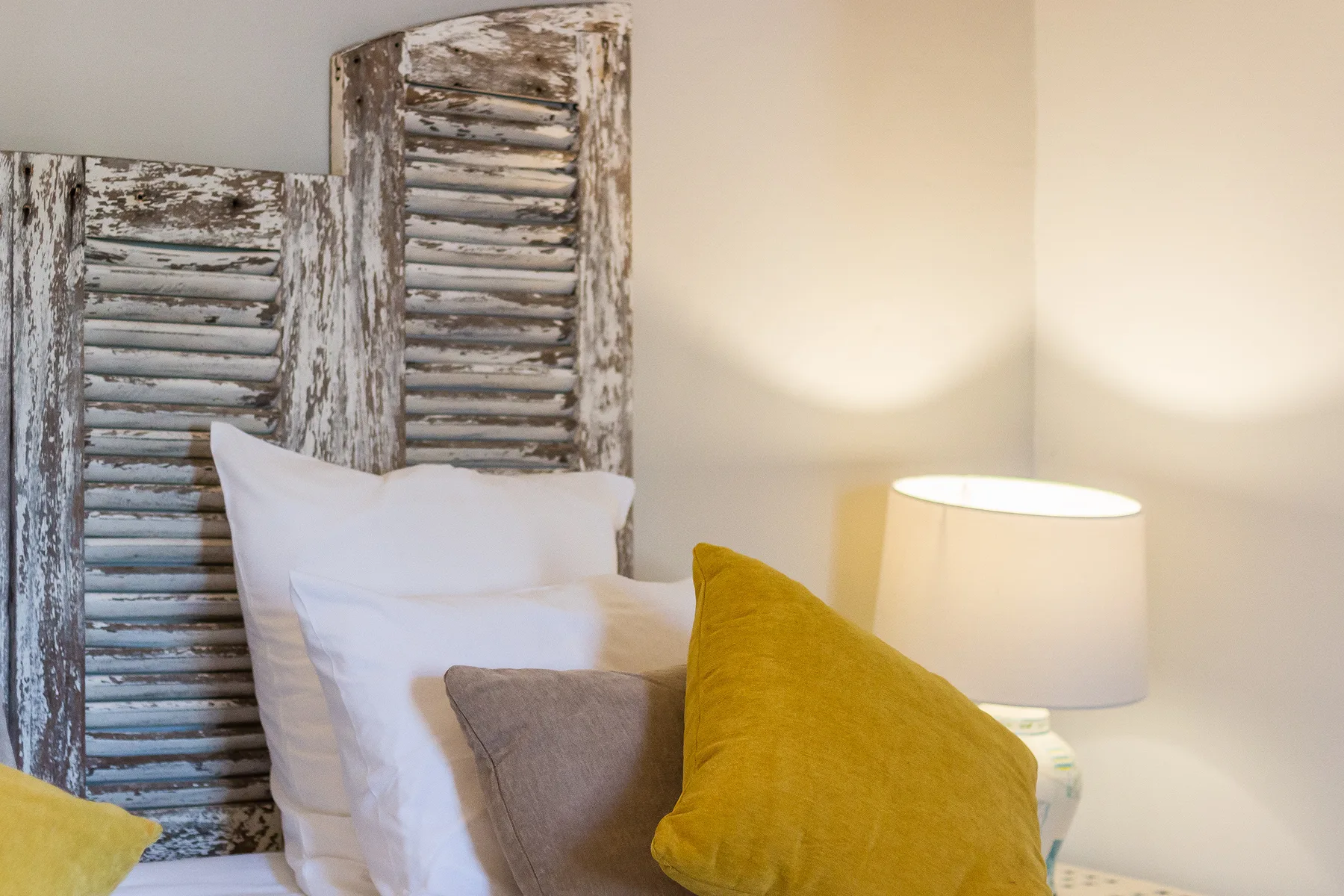 Un dormitorio con ropa de cama blanca y cojines de colores junto a una lámpara encendida.