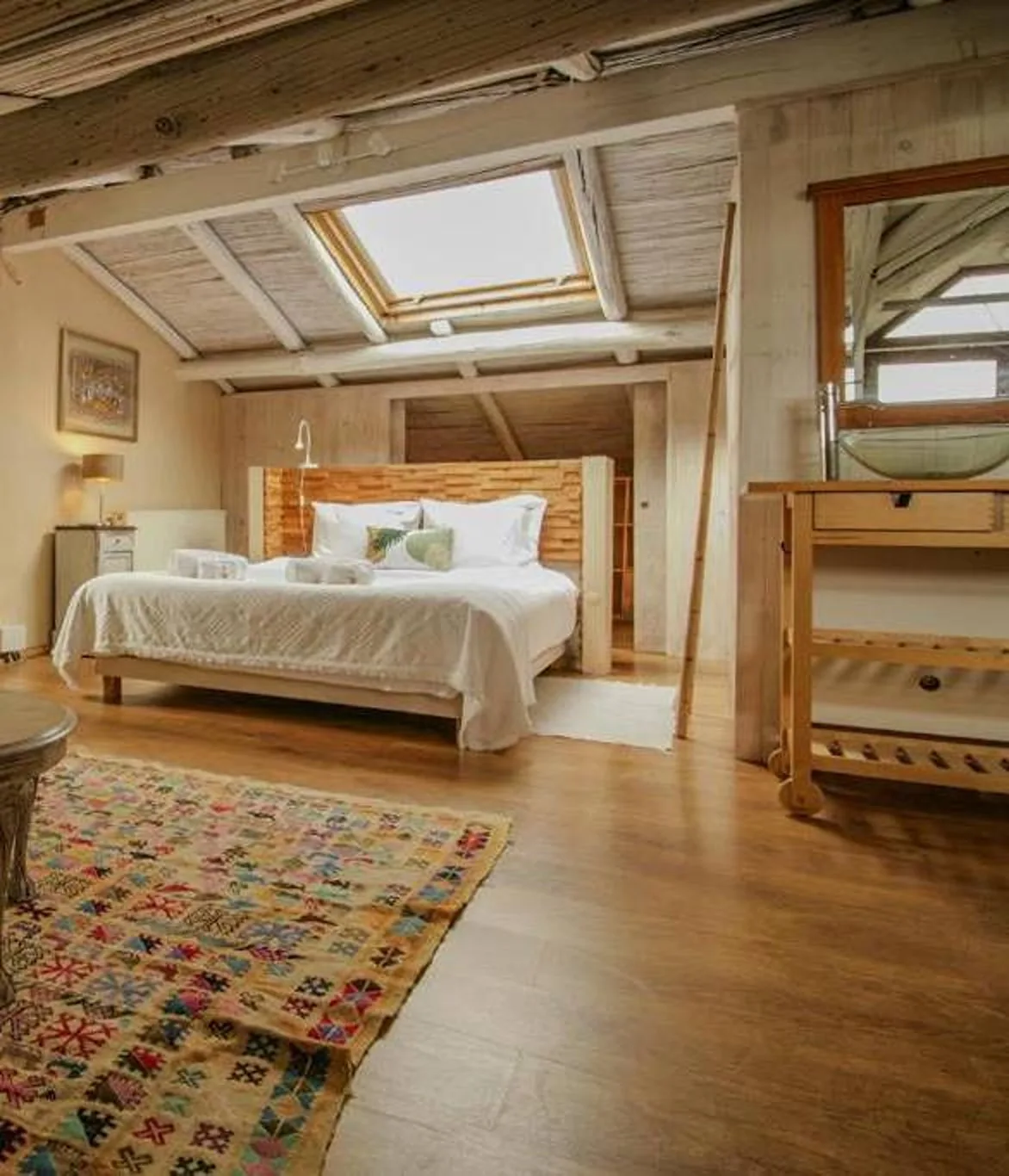A bedroom with a bed beneath a skylight and a colorful rug.