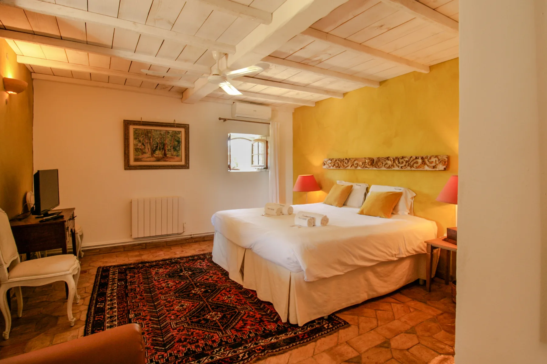 A bedroom with a large bed, colorful rug, and warm yellow walls.