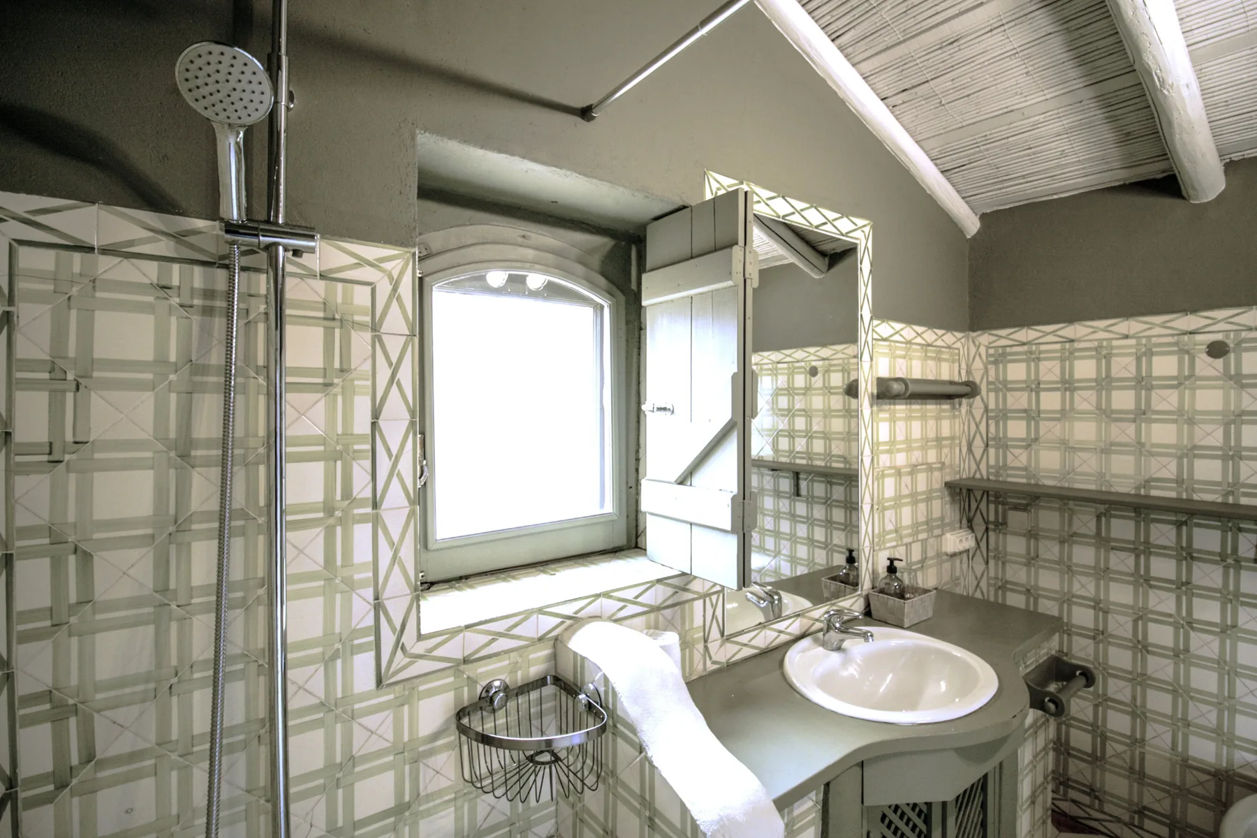 Un baño con azulejos, ducha, lavabo y una ventana luminosa.