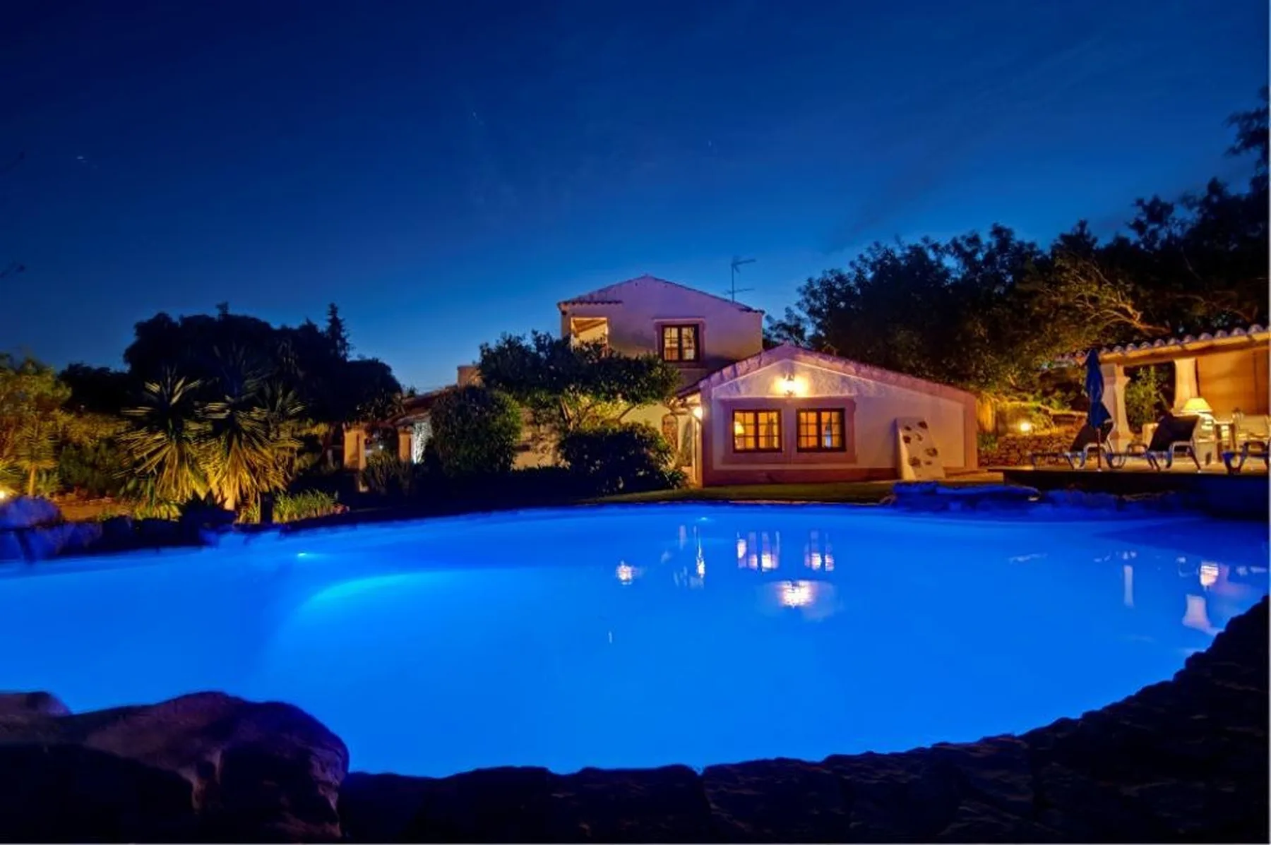 Una piscina iluminada está frente a una casa al anochecer.