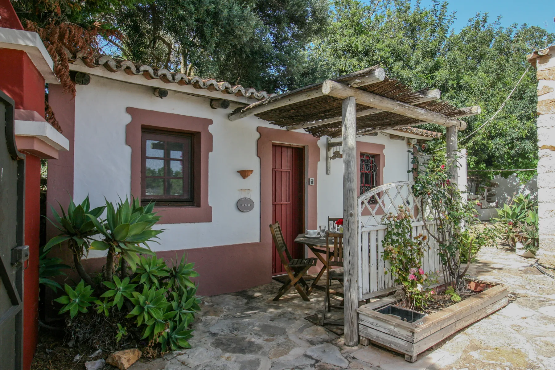 Una casa blanca de estuco da a un patio de piedra bajo una pérgola de madera.