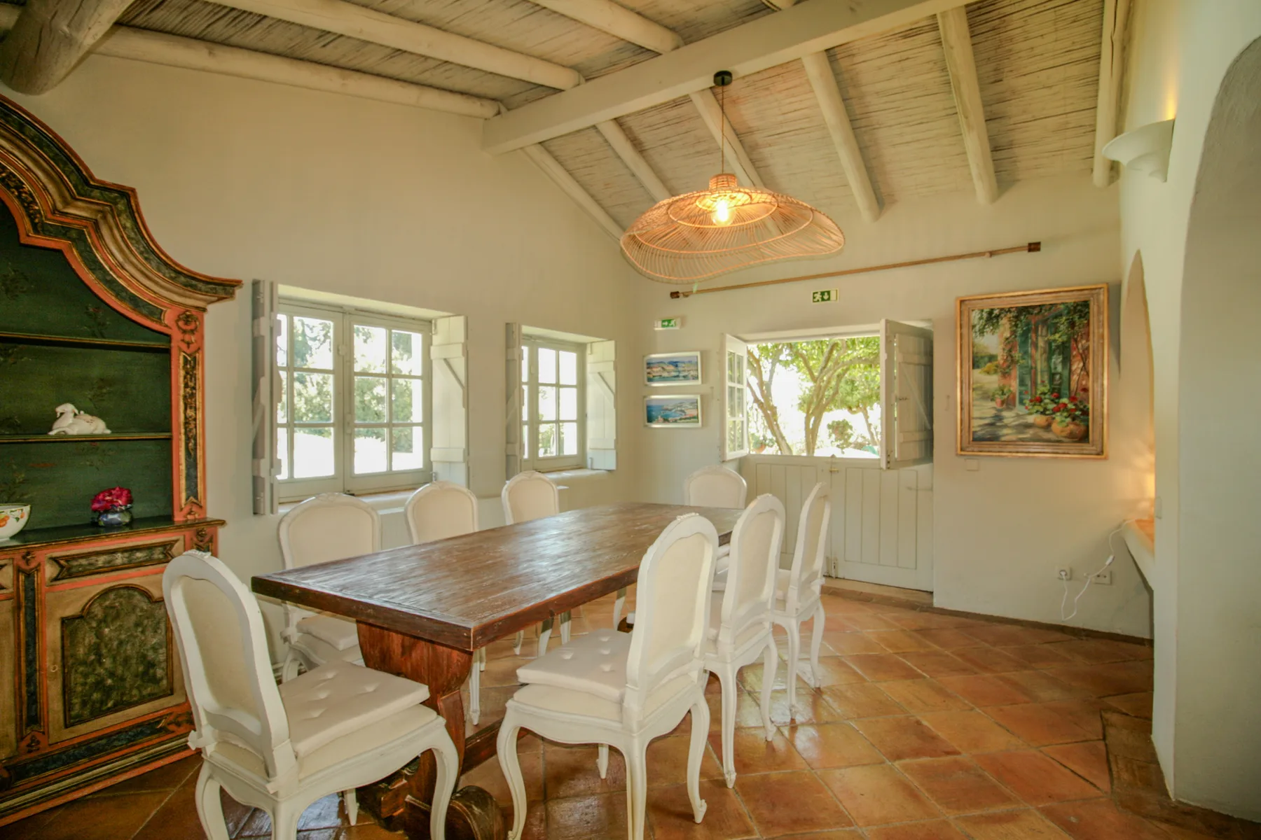 Comedor con una mesa de madera, asientos blancos y una ventana grande.