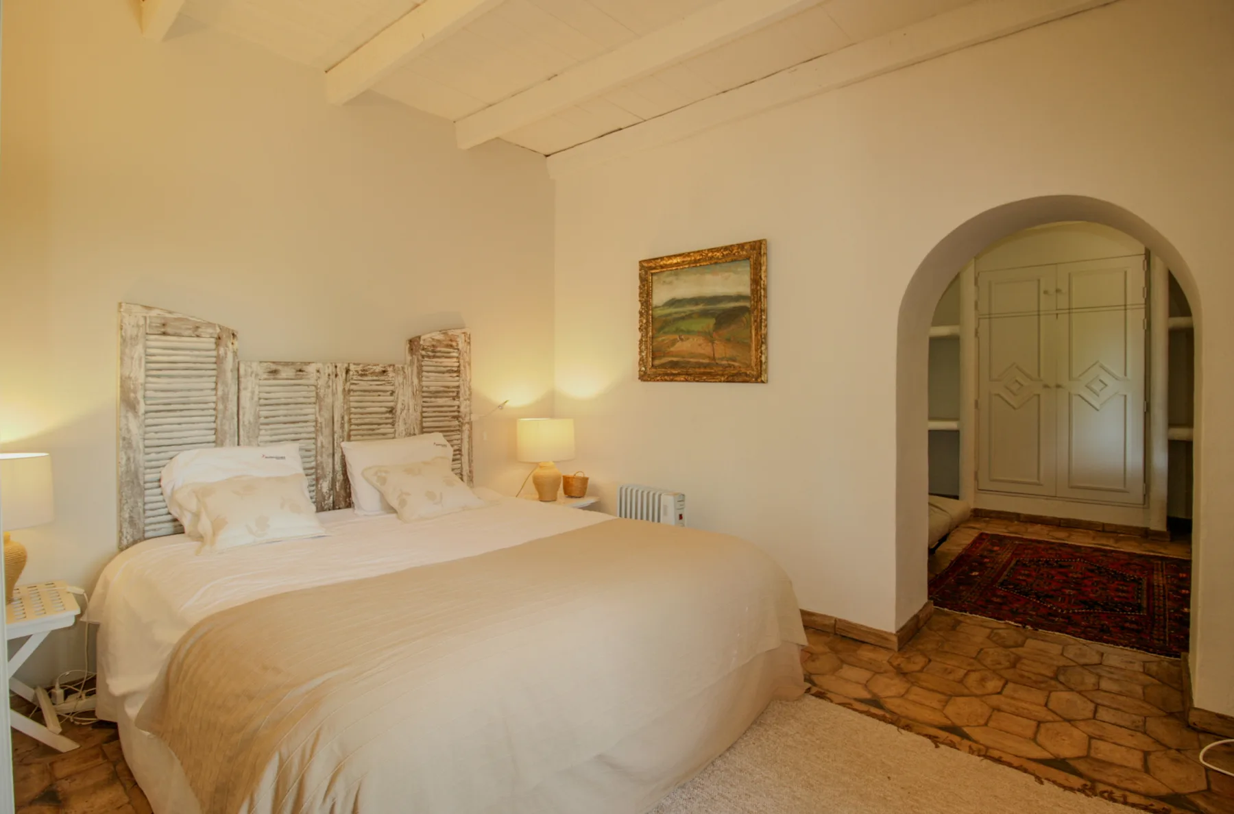 A bedroom with a large bed, bedside lamps, and an arched doorway.