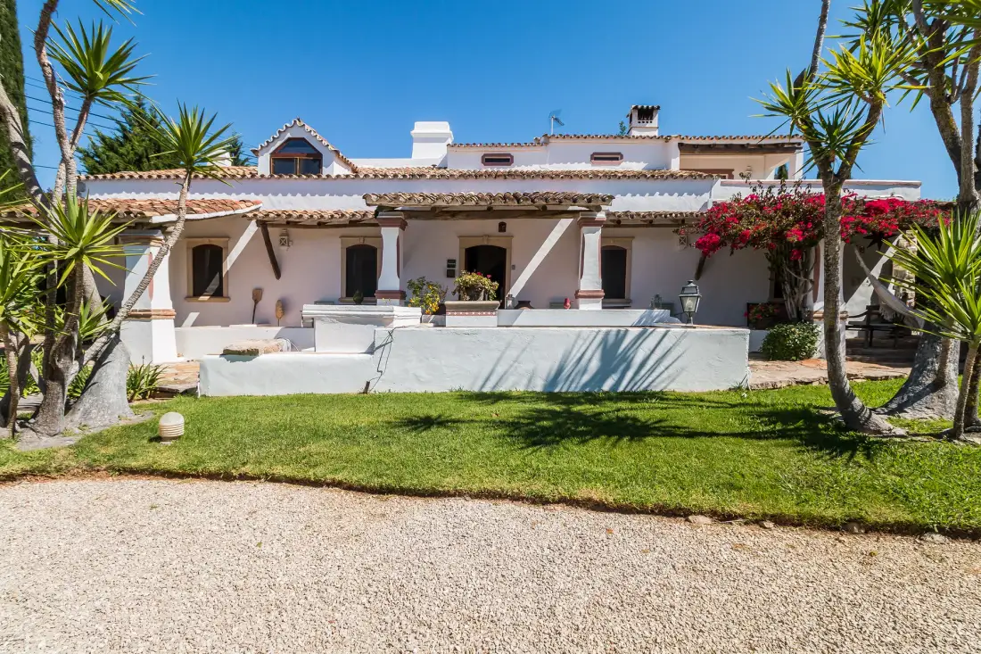 Una villa blanca se alza detrás de un césped y un camino de grava.