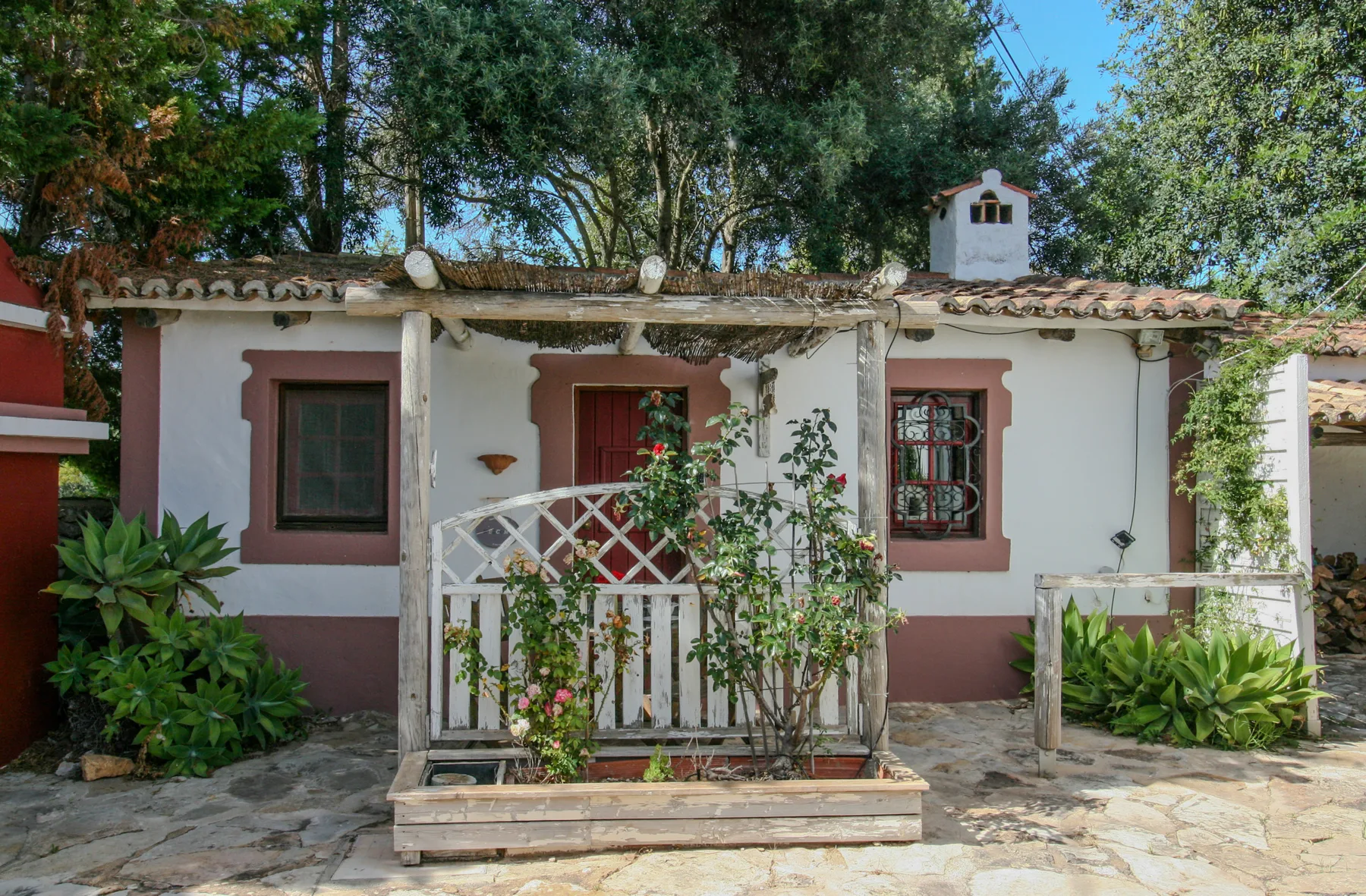 Exterior de una casa blanca con entrada central, plantas trepadoras y patio de piedra.