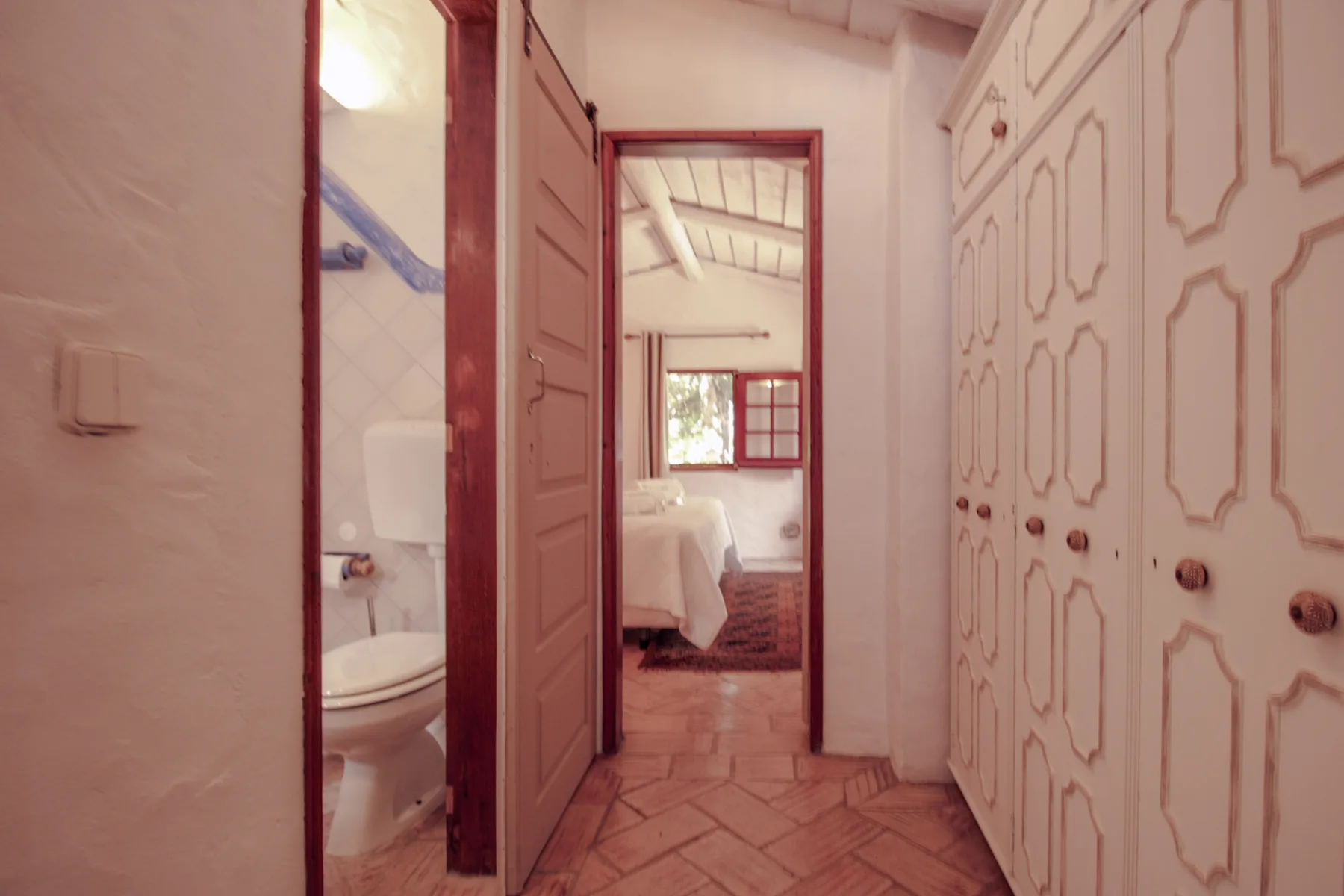 Un pasillo con armarios empotrados y puertas abiertas hacia un dormitorio y un baño.