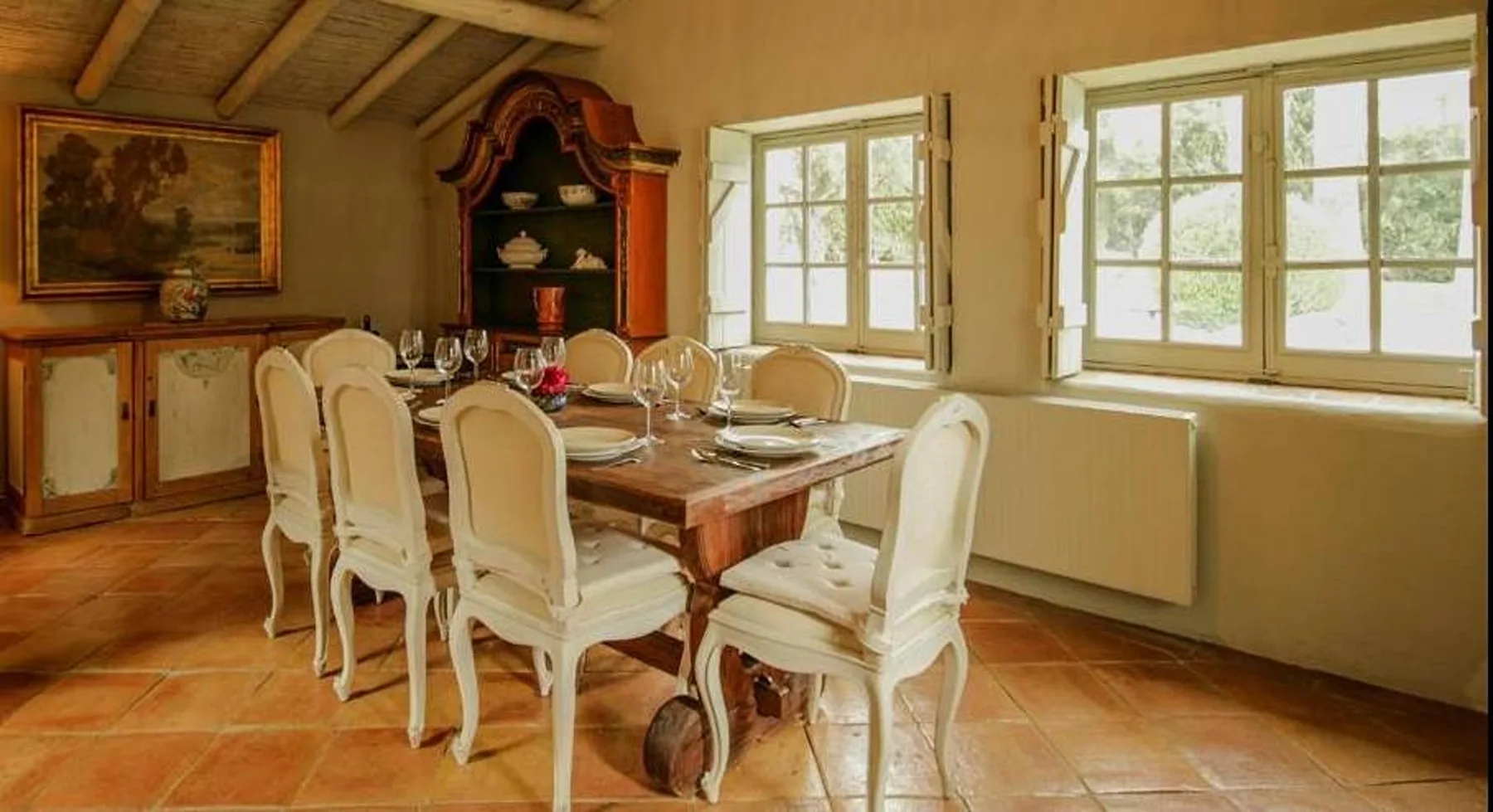 Un comedor con una mesa larga y sillas junto a ventanas luminosas.