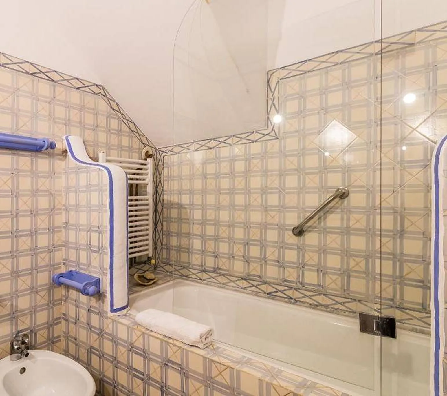 Un baño alicatado con una bañera y una toalla apoyada en el borde.
