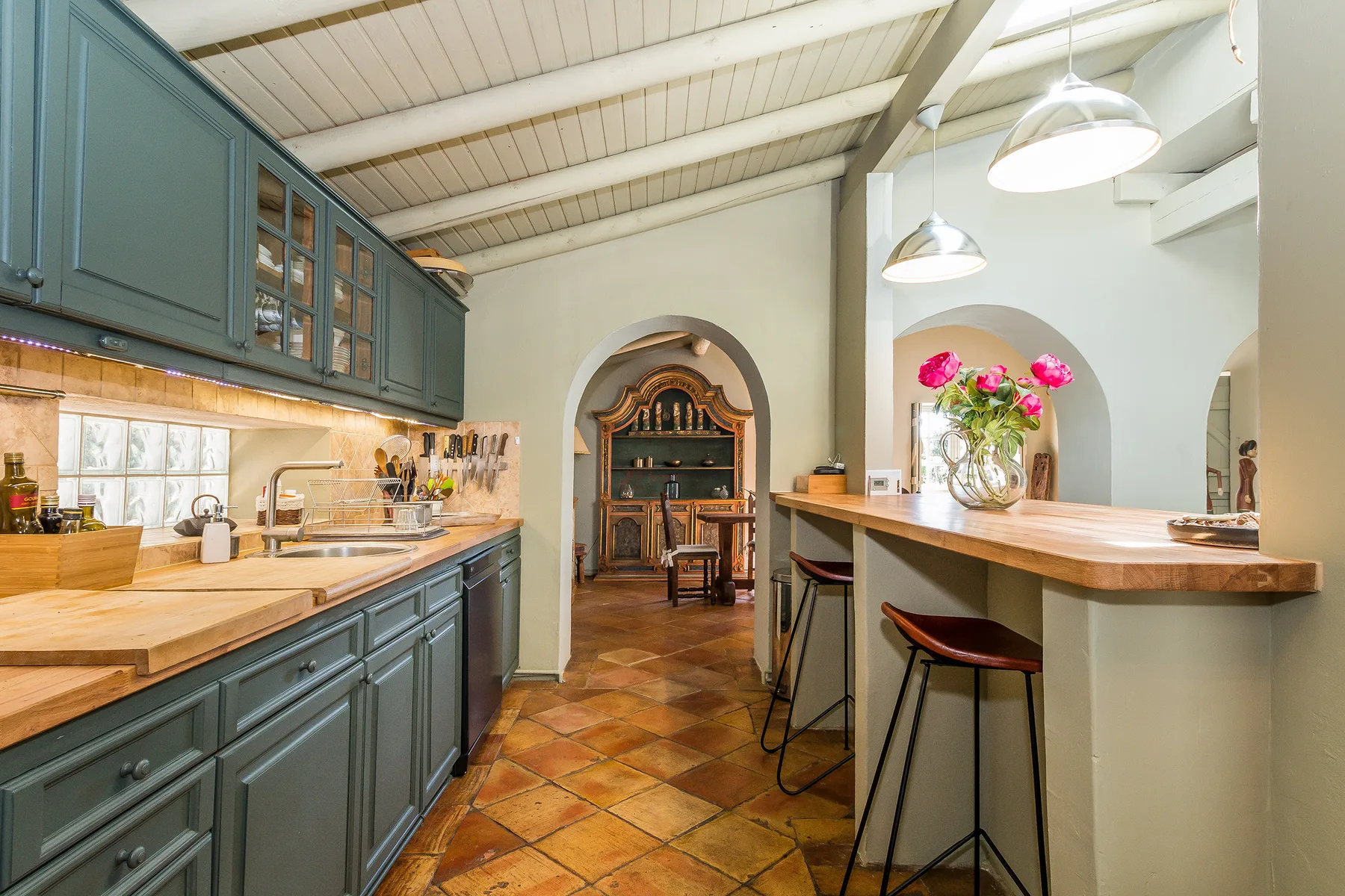 Una amplia cocina con muebles verdes, suelo de baldosas y una isla con encimera de madera.