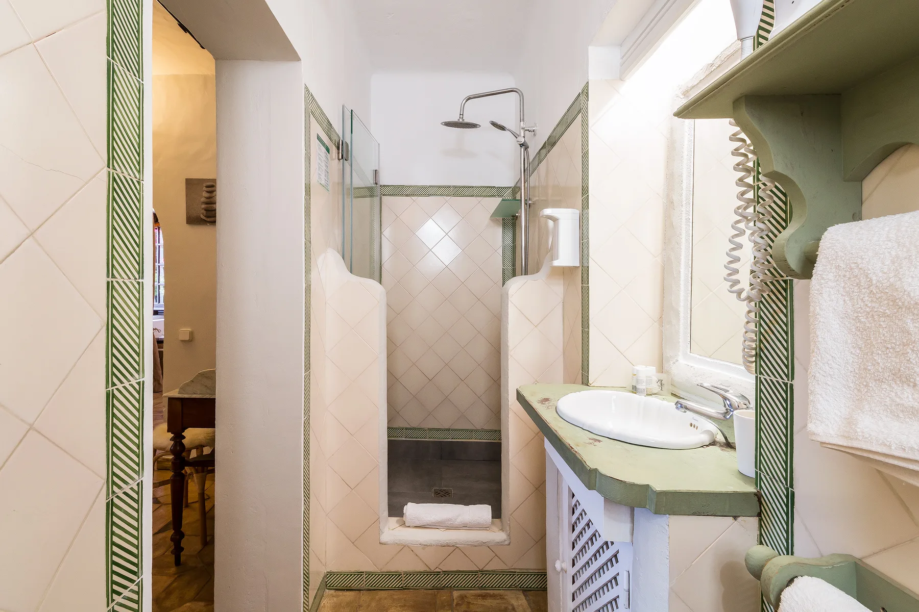 Un baño alicatado tiene una ducha y un tocador verde con lavabo.