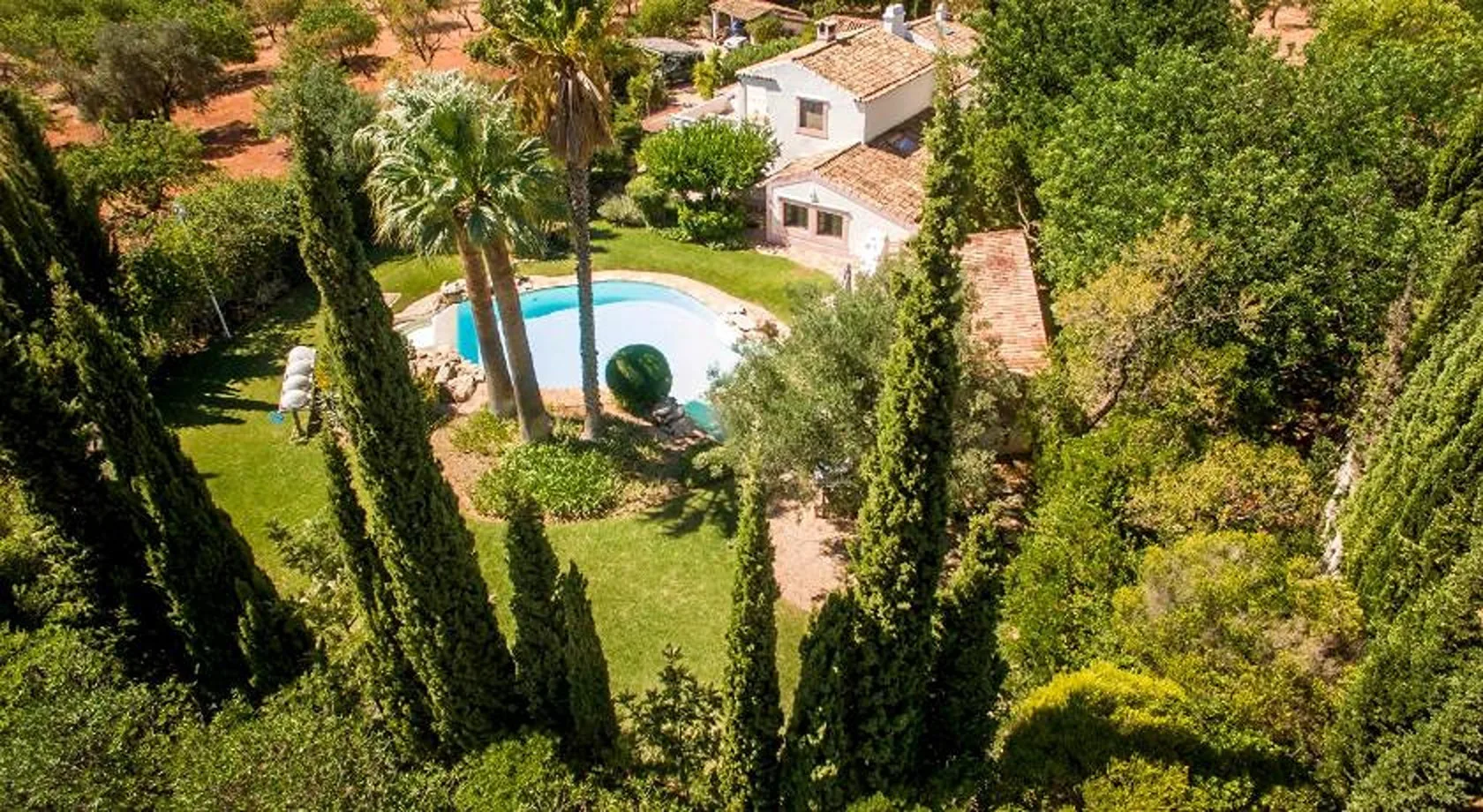 Vista aérea de un jardín ajardinado con piscina y edificios cercanos.