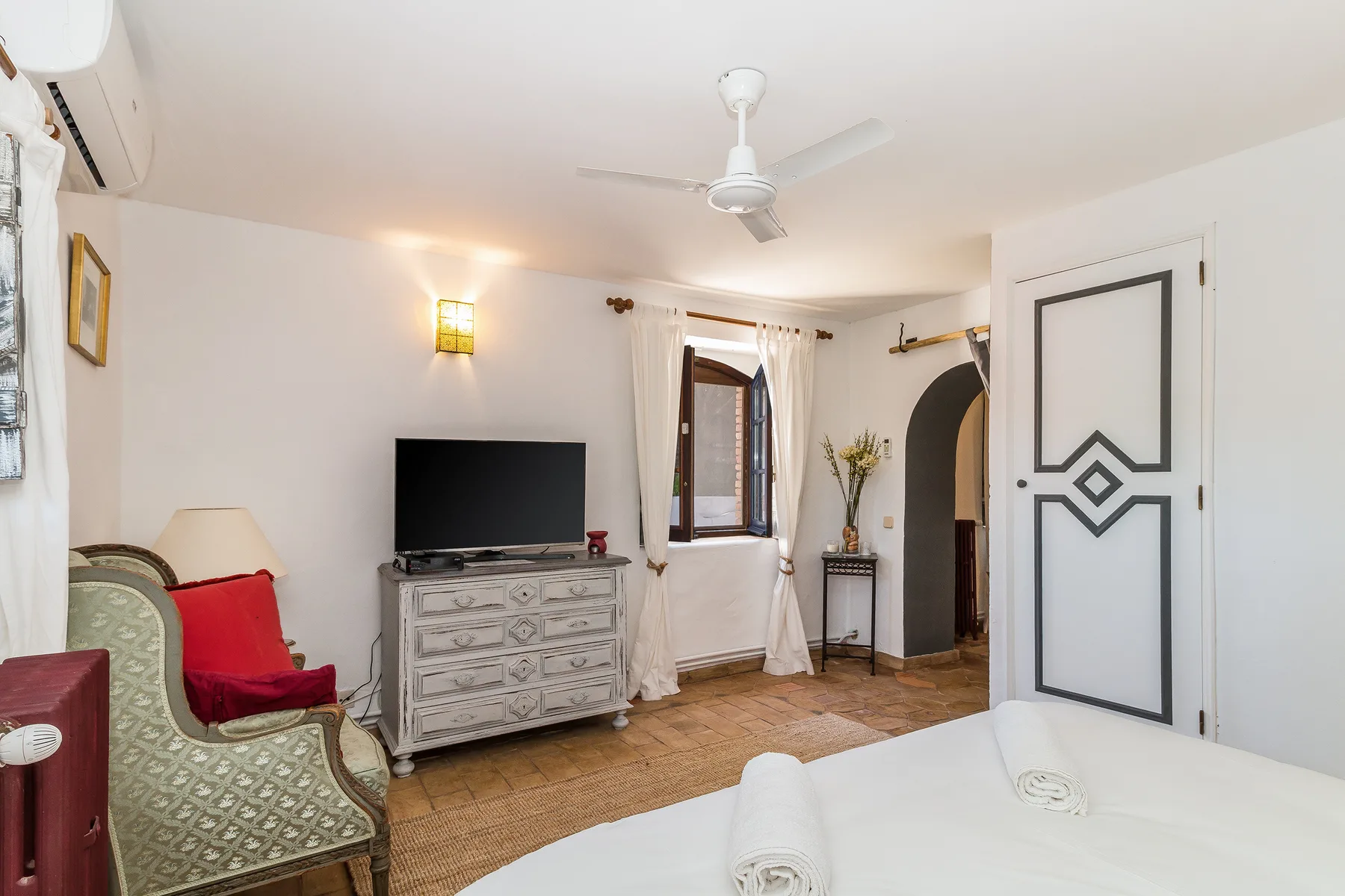 Dormitorio con televisión, asientos y una cama en primer plano.