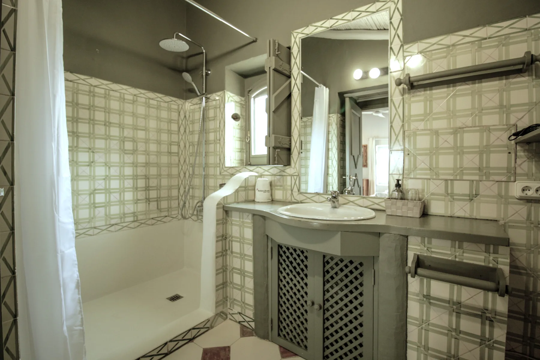 Un baño alicatado con ducha, lavabo y un espejo grande.
