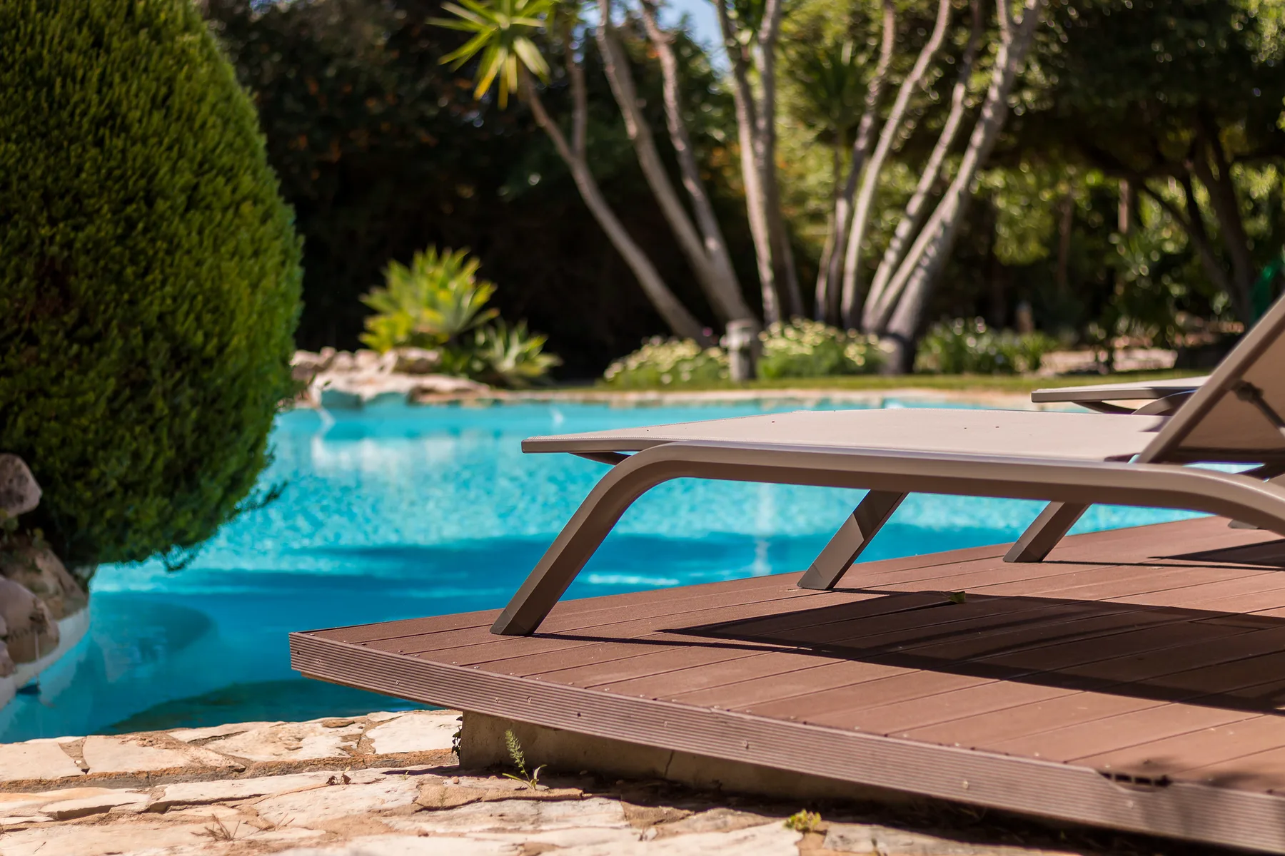 Una piscina junto a una terraza de madera con tumbonas reclinables.