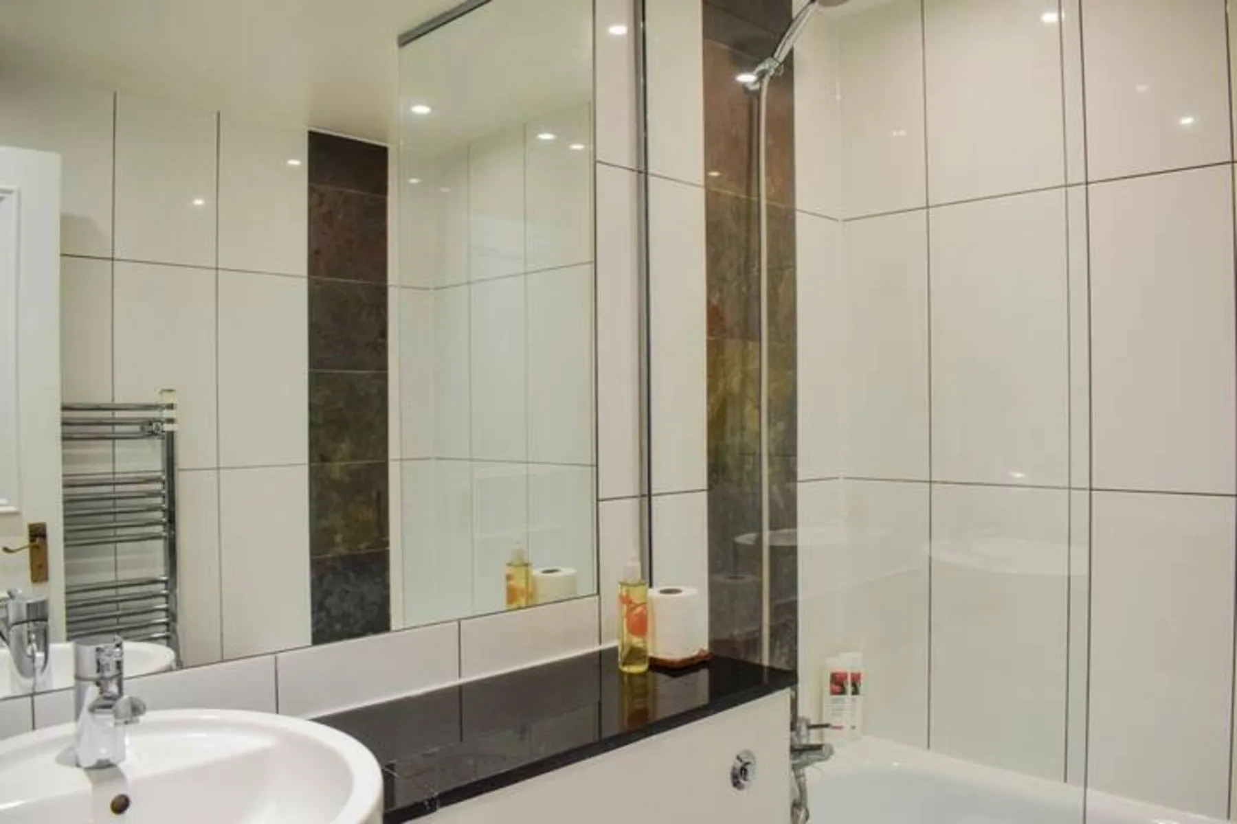 A tiled bathroom with a large mirror, sink, and bathtub.