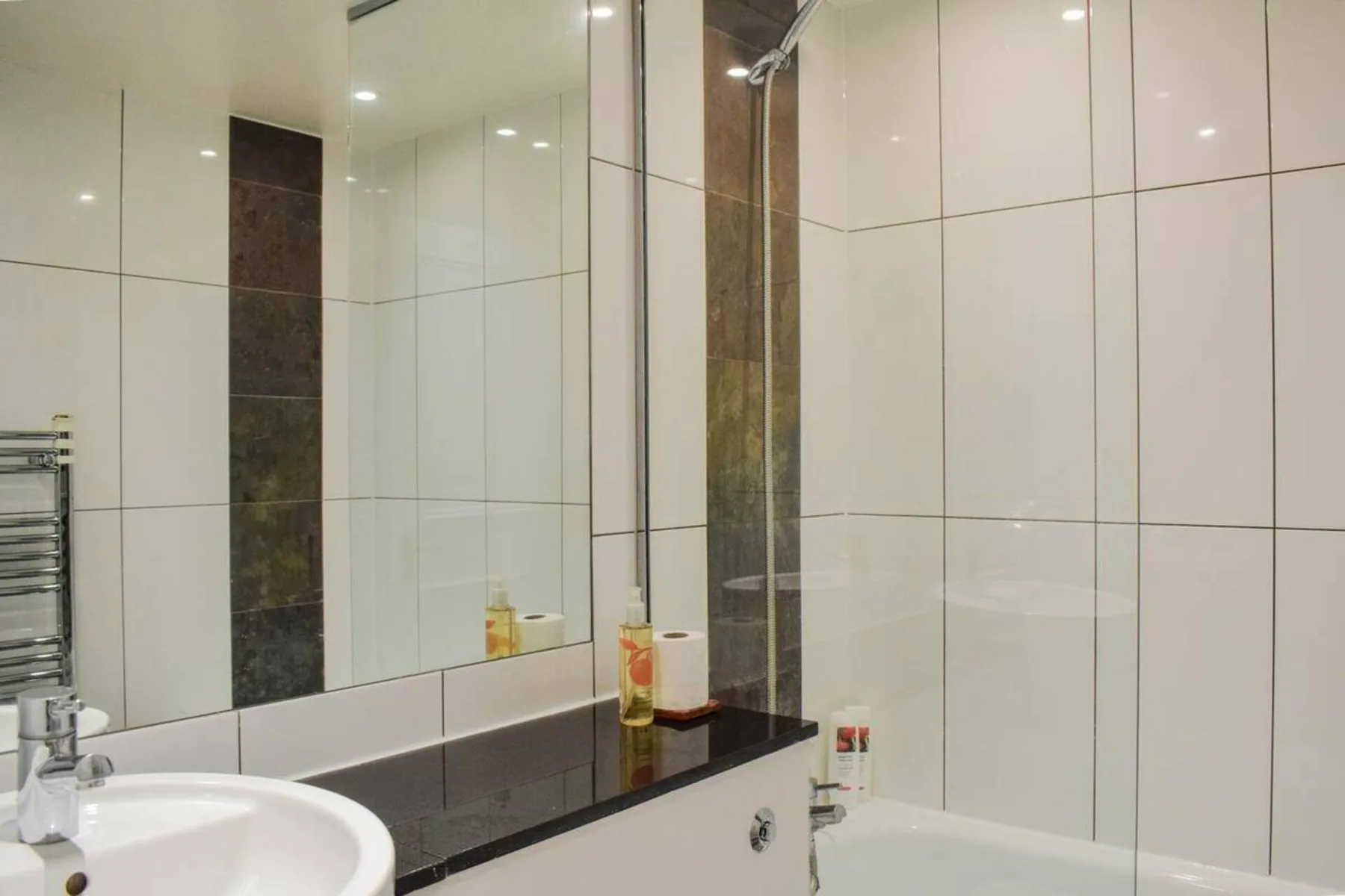 A tiled bathroom with a sink, mirror, and bathtub.