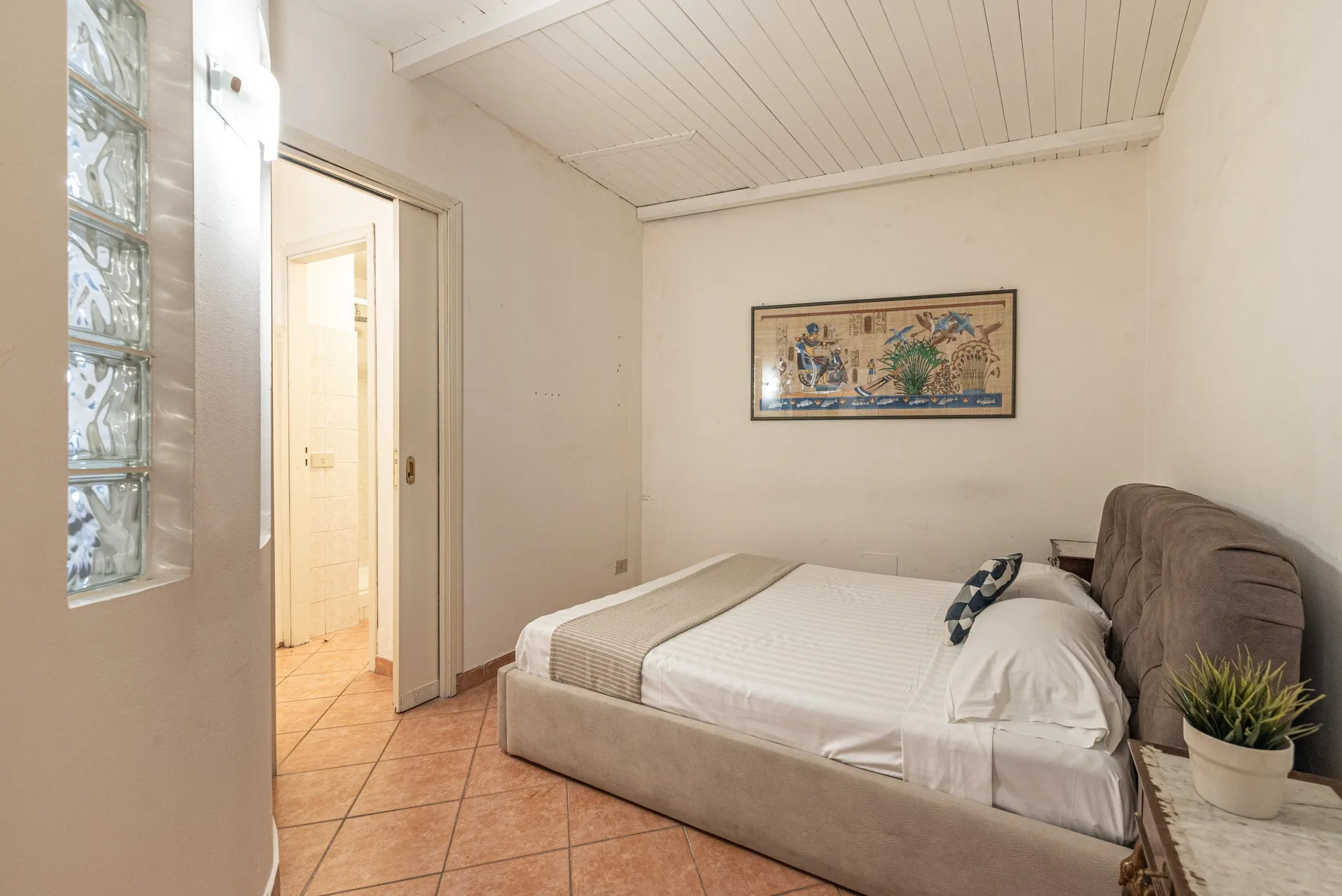 Un dormitorio con una cama, un cuadro enmarcado y una puerta abierta.