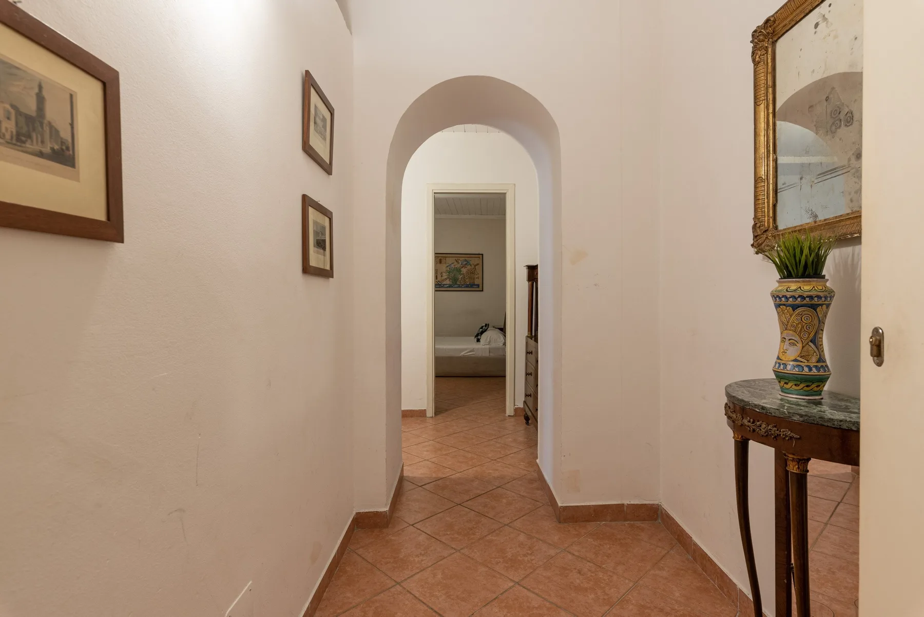 A tiled hallway with an arched doorway and framed pictures.