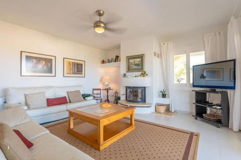 A bright living room has seating around a wooden coffee table and fireplace.