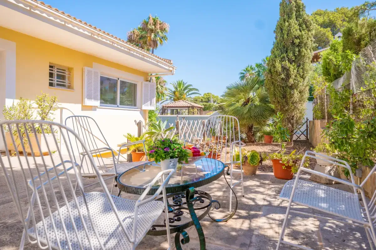 A sunny patio with outdoor seating, a glass table, and potted plants.