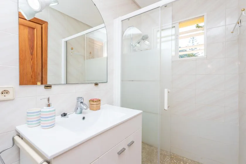 A bright bathroom with a sink, mirror, and glass shower.