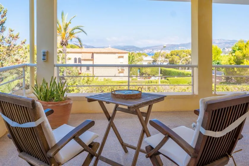 A covered balcony with seating and a small table overlooks surrounding homes and hills.