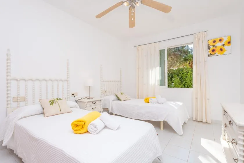 A bright bedroom with two beds and a window overlooking greenery.