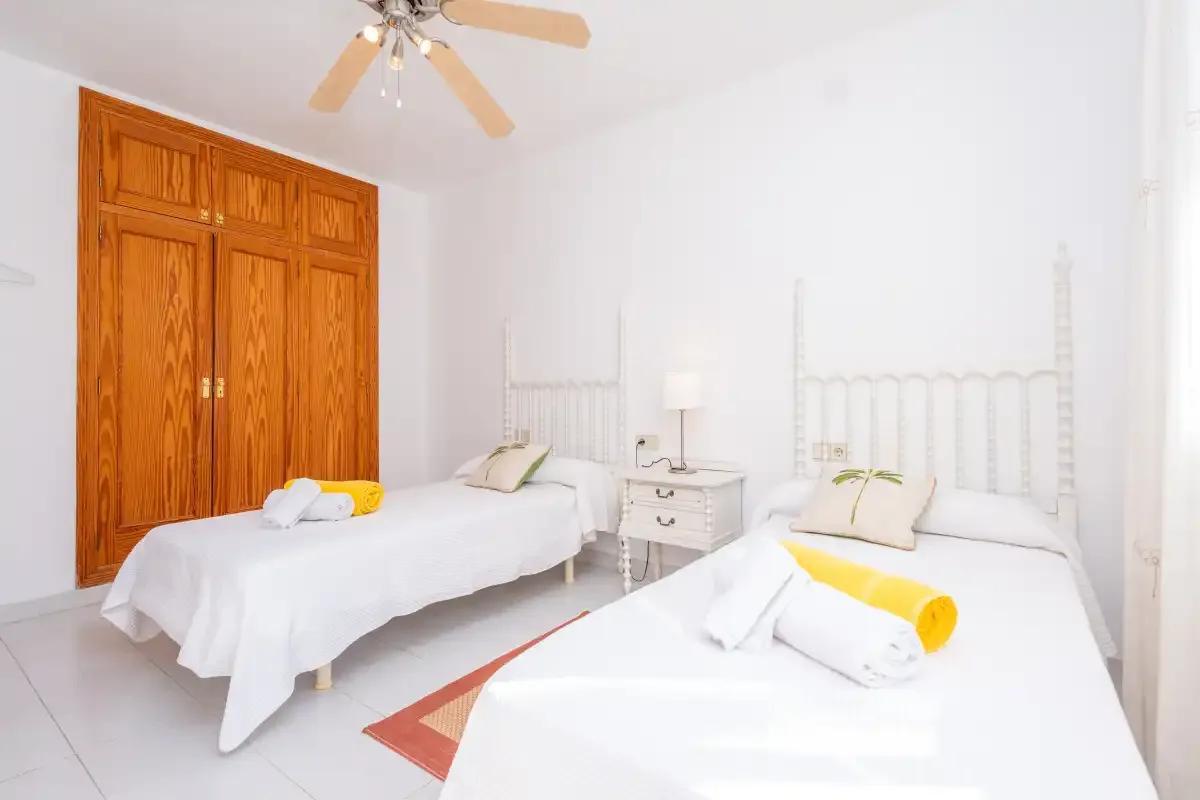 A bright bedroom with two beds, white bedding, and a wooden wardrobe.
