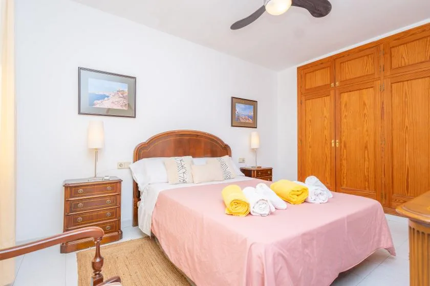 A bedroom with a bed dressed in pink and wooden wardrobes.